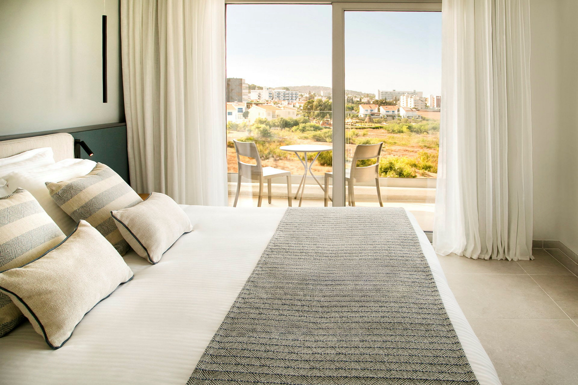Hotellrum med en dubbelsäng och utgång till balkong med bord och stolar. (AI-genererad text)