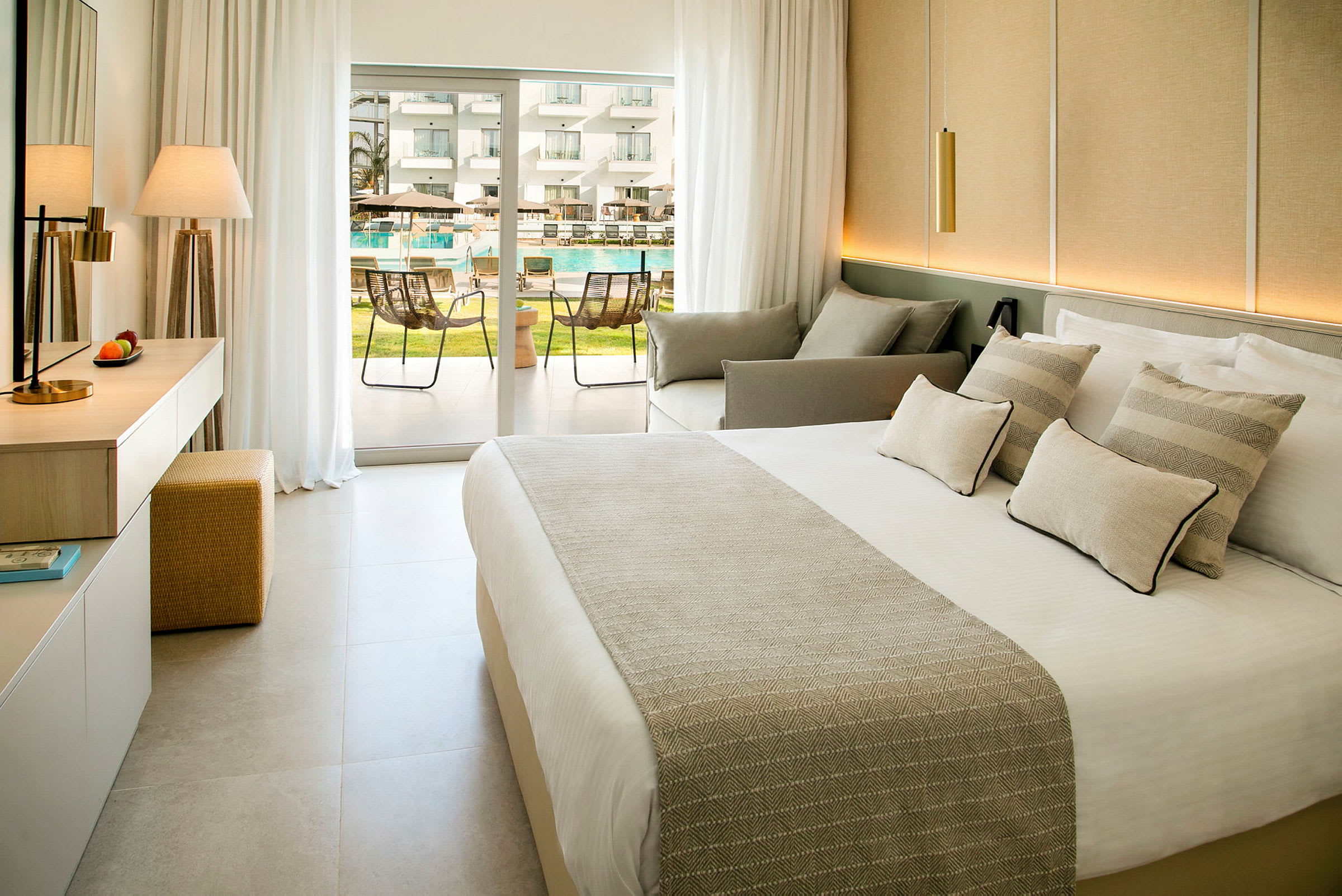 Modernt hotellrum med säng, sittgrupp och fransk dörr mot poolområde. (AI-genererad text)