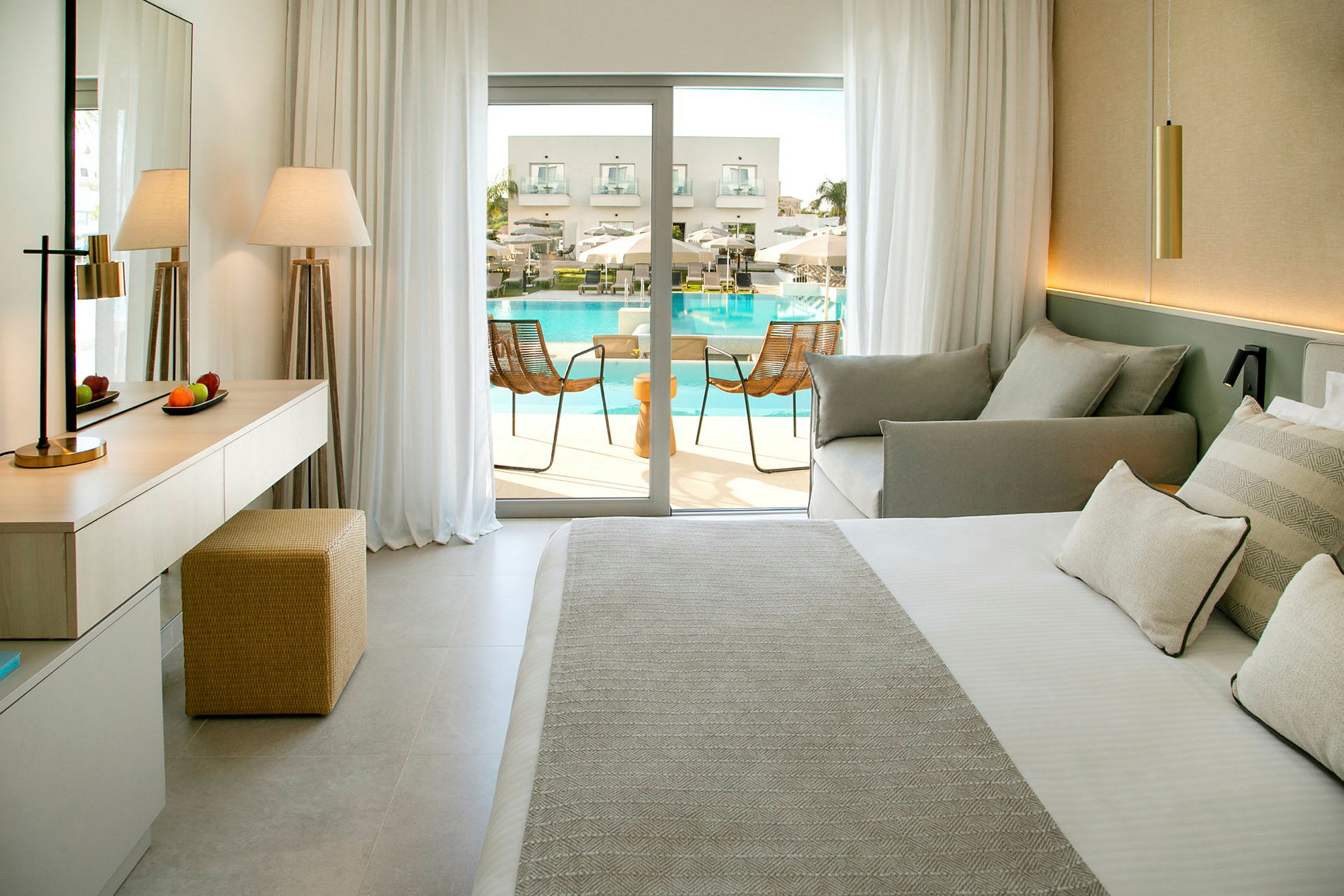 Ett hotellrum med säng, soffa och utgång till en balkong med vy mot poolområdet. (AI-genererad text)