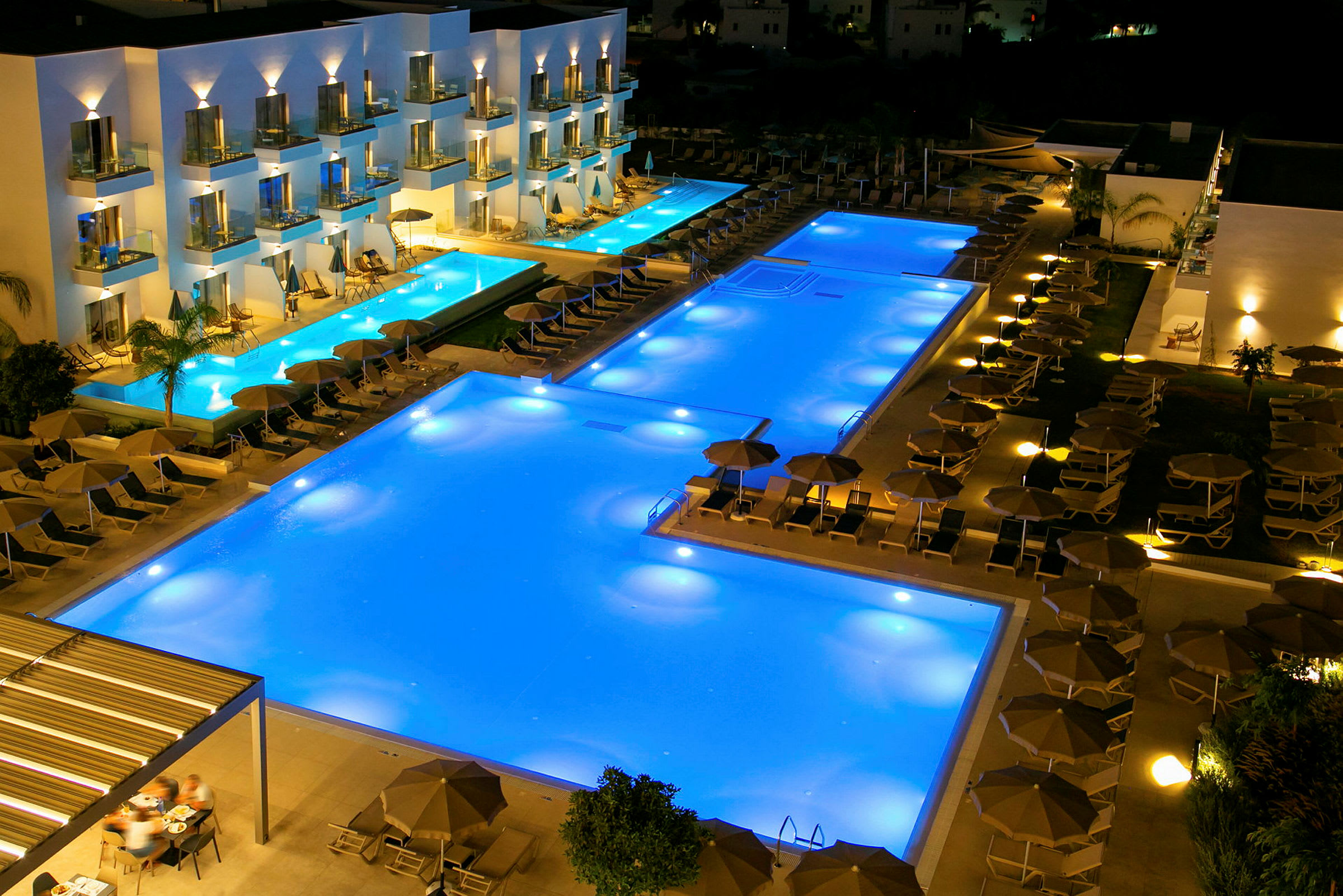 En poolanläggning vid ett hotell på kvällen med belysta pooler och solstolar. (AI-genererad text)