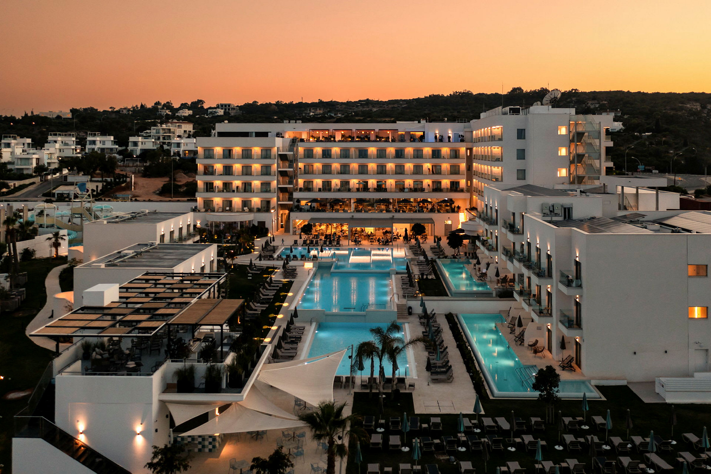 Hotellanläggning i skymningen med pooler och belysning. (AI-genererad text)