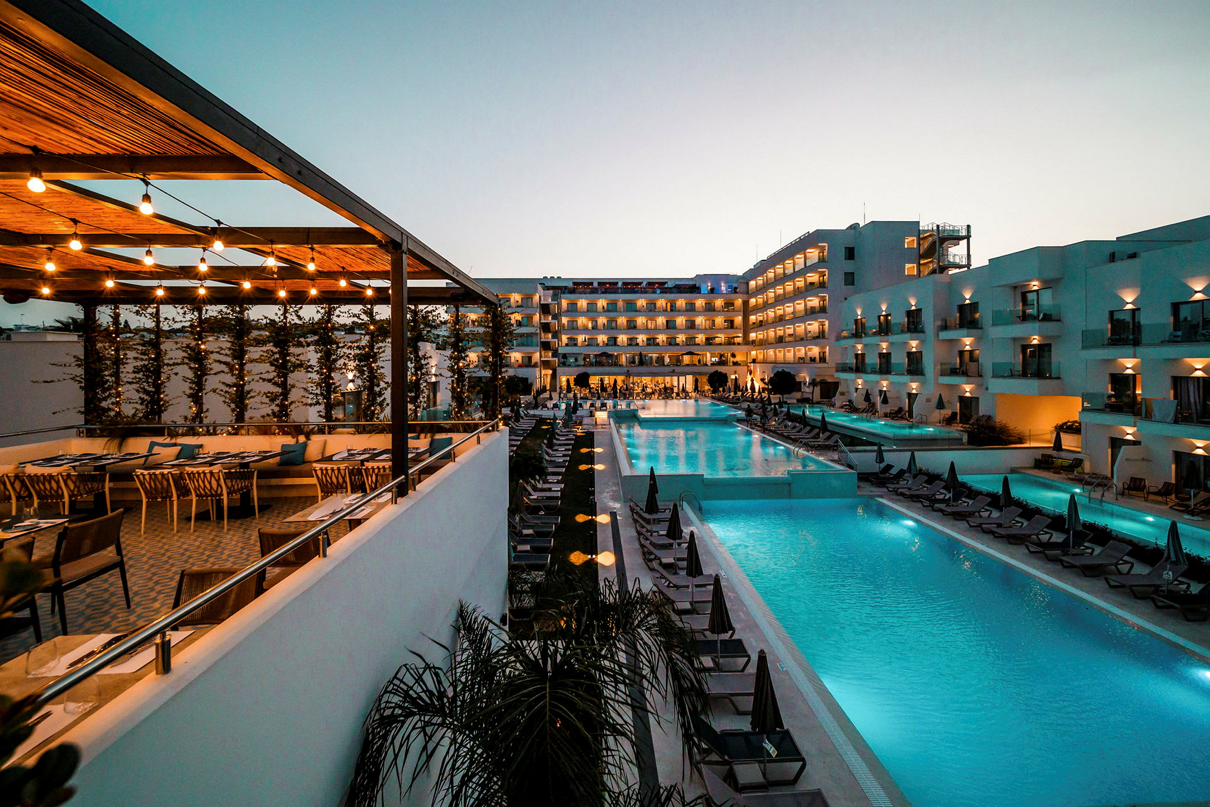 Bild av ett hotellområde med pool och sittplatser vid solnedgången. (AI-genererad text)