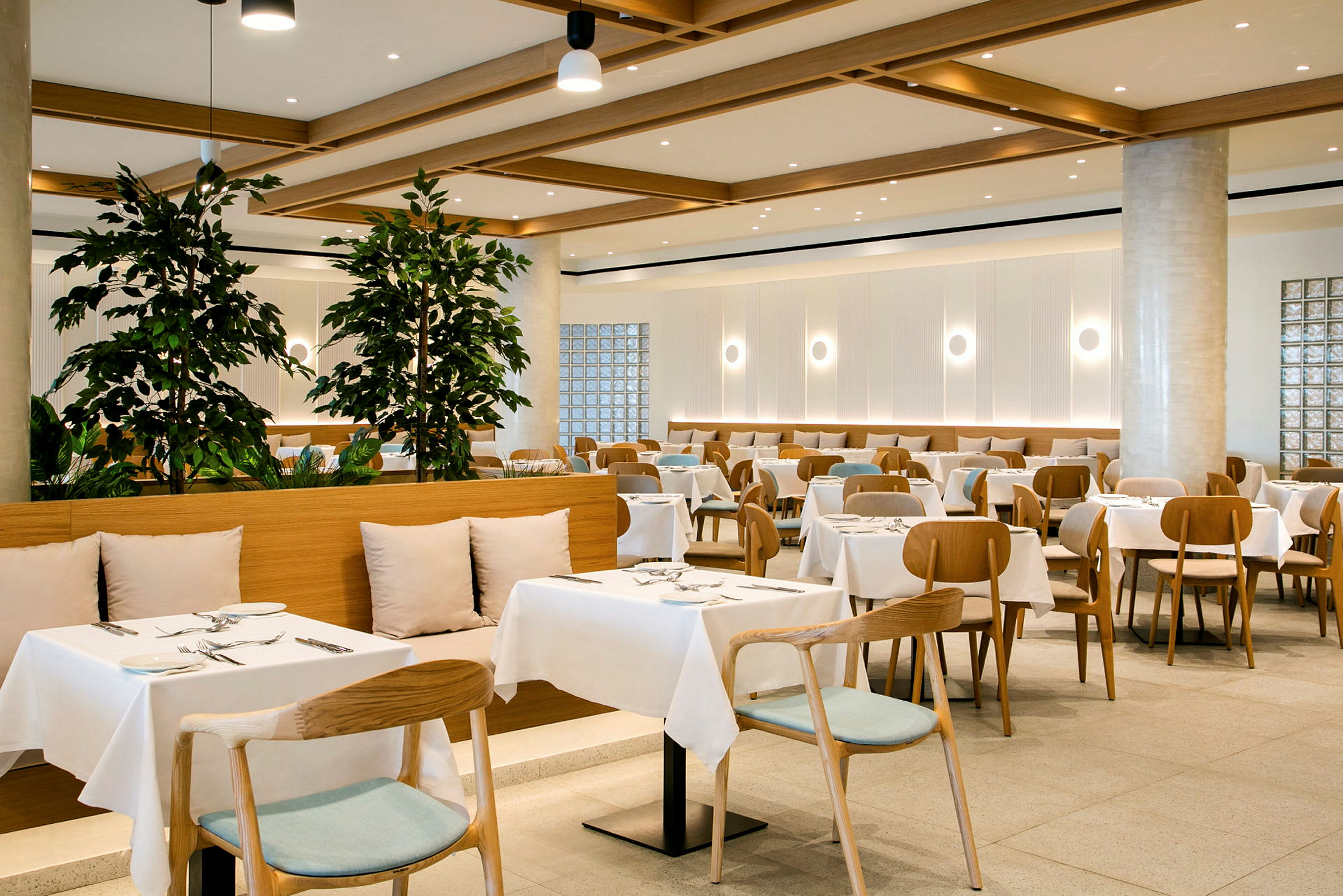 En modern restaurang med uppsatta bord och stolar, dekorerad med gröna växter. (AI-genererad text)