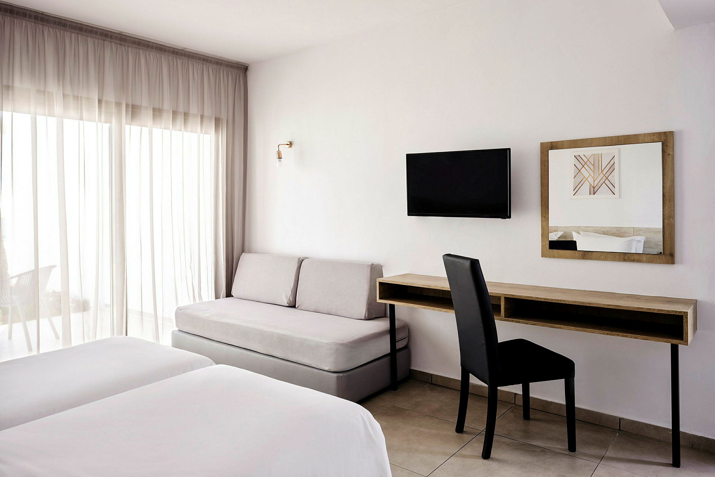 Ett hotellrum med två sängar, en soffa, ett skrivbord och en väggmonterad TV. (AI-genererad text)