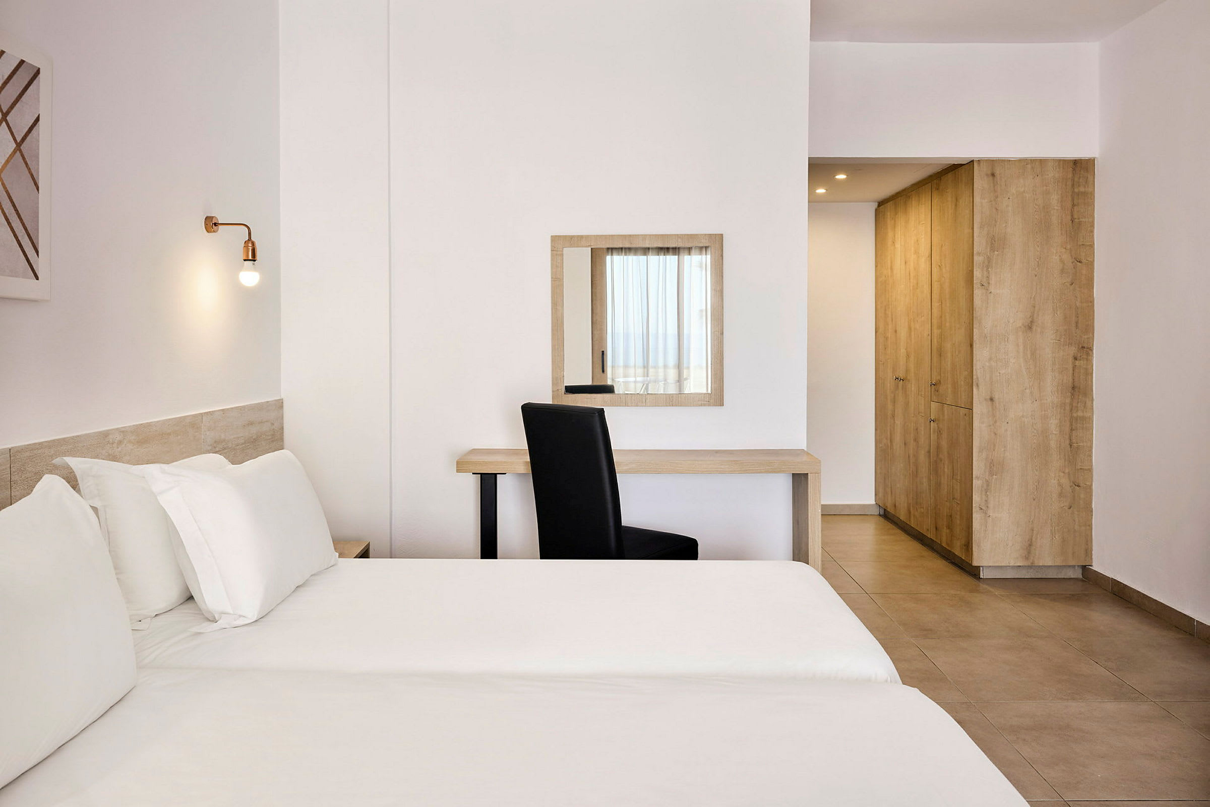 Ett ljust hotellrum med en säng, skrivbord, stol och garderob. (AI-genererad text)