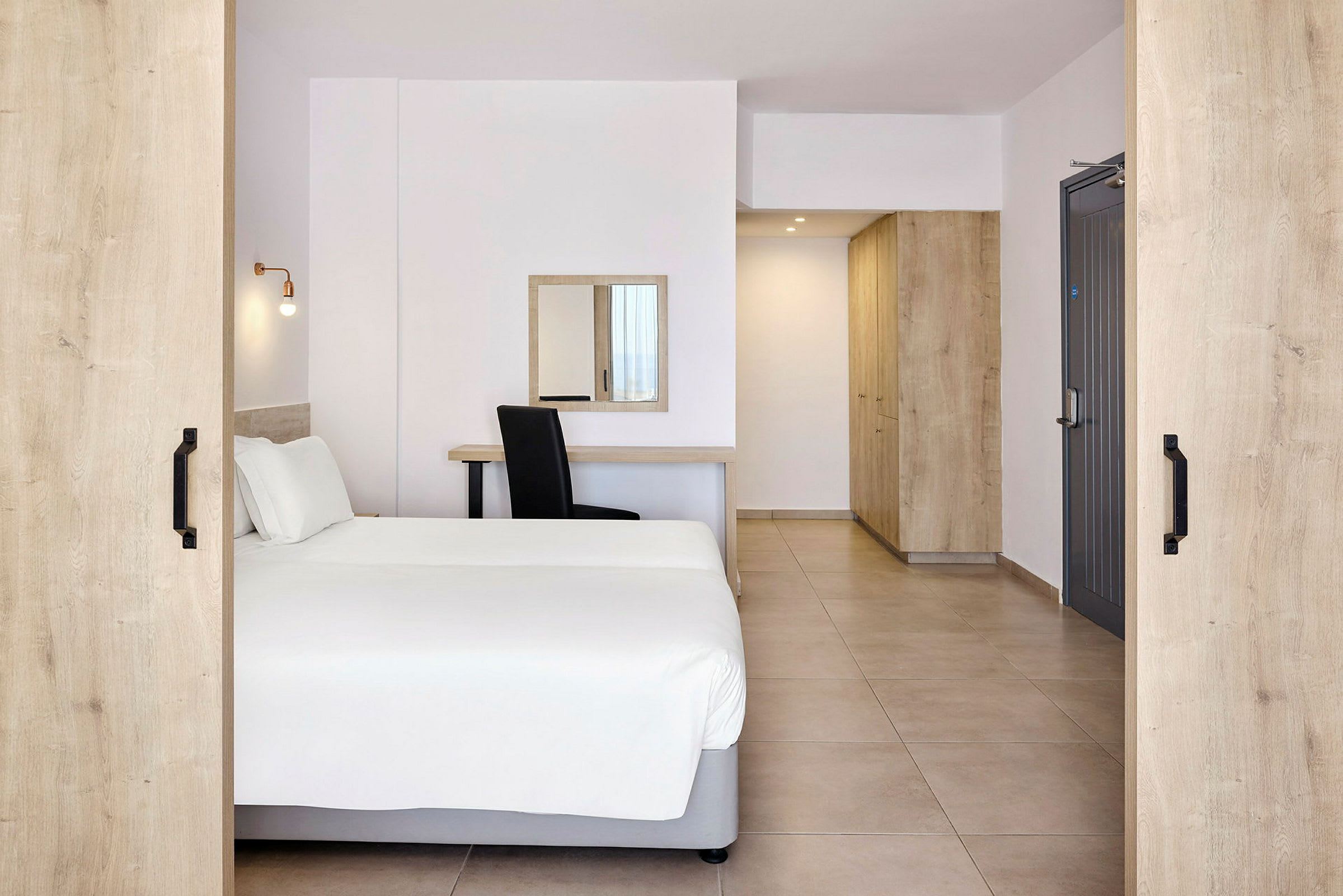Ett hotellrum med en dubbelsäng, skrivbord, spegel och förvaringsmöbler. (AI-genererad text)
