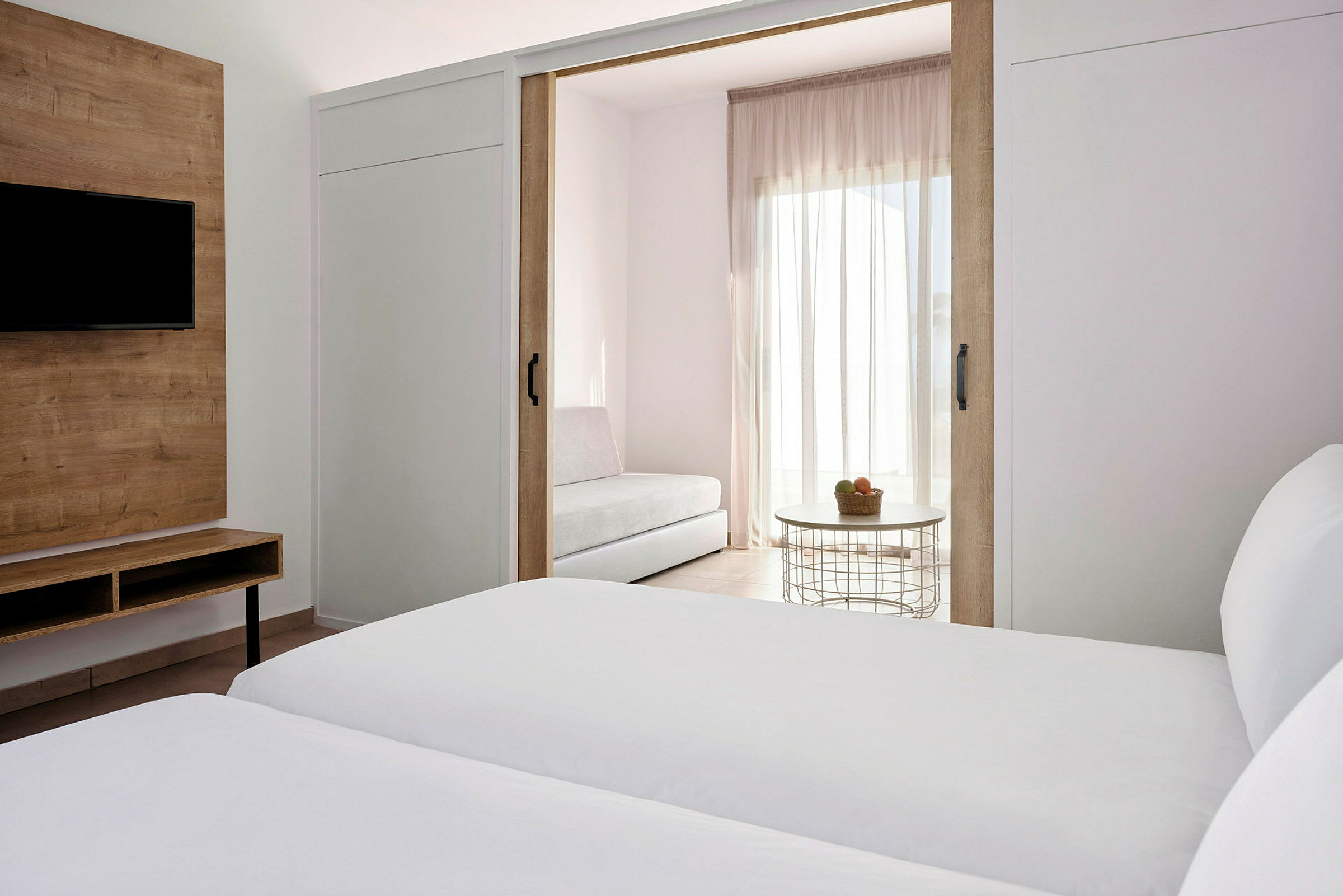 Ett hotellrum med separata sängar, en TV på en trämöbel och en sittgrupp bakom skjutdörrar. (AI-genererad text)
