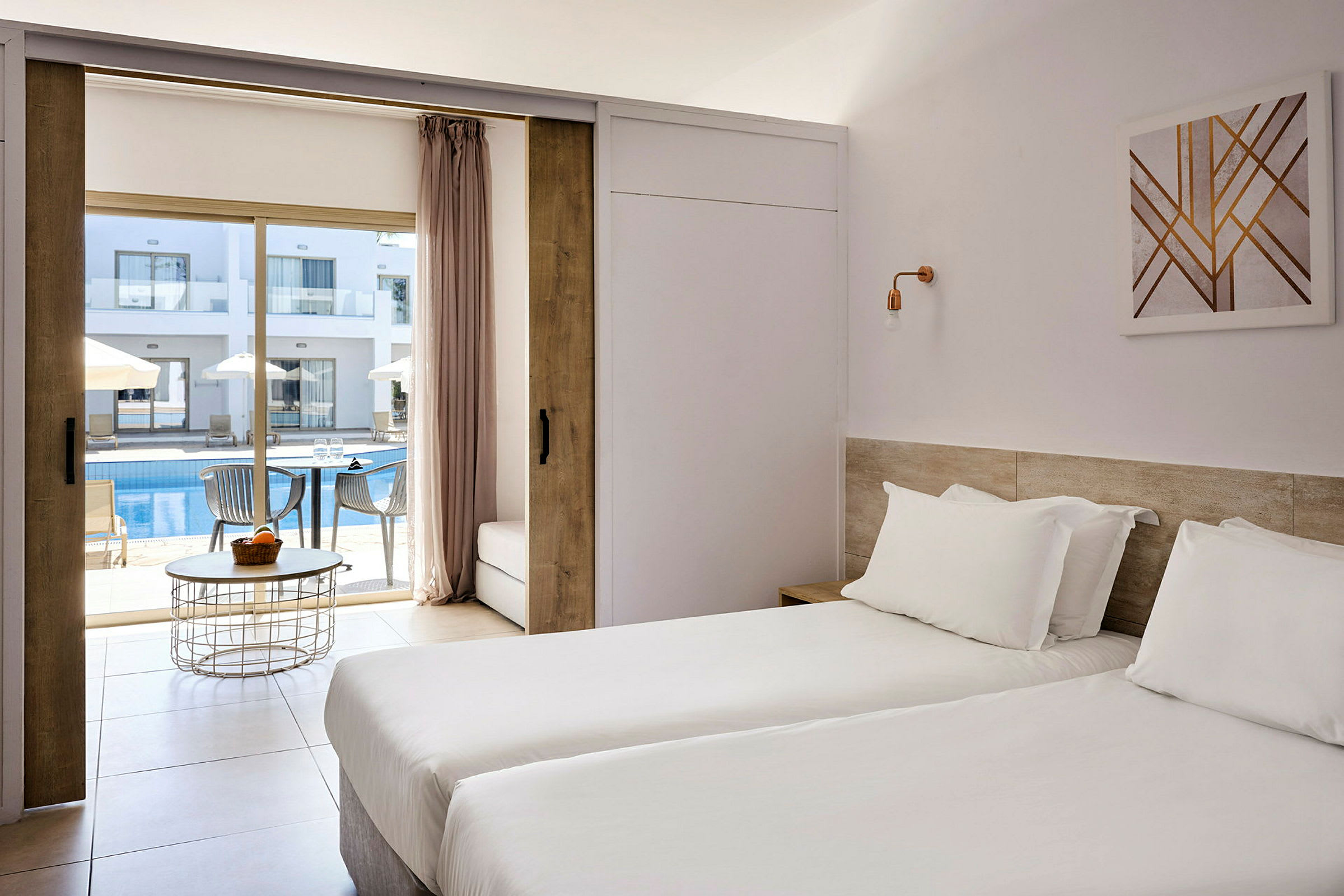 Hotellrum med två enkelsängar och utsikt mot en utomhuspool och solstolar. (AI-genererad text)
