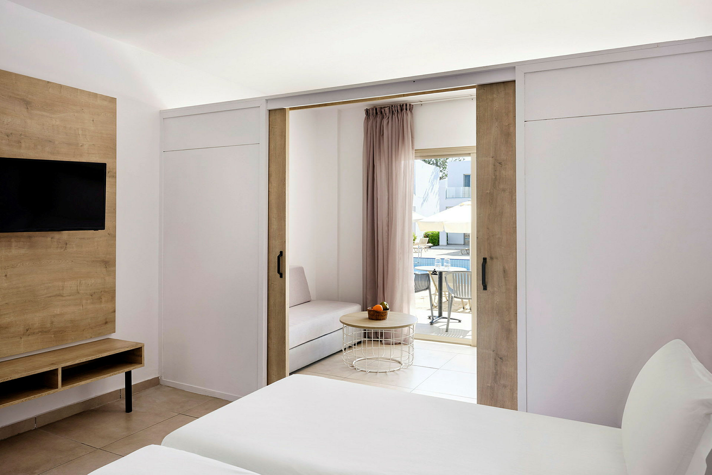 Hotellrum med enkelsängar, ett vardagsrum och utsikt över en terrass tillhörande poolområdet. (AI-genererad text)