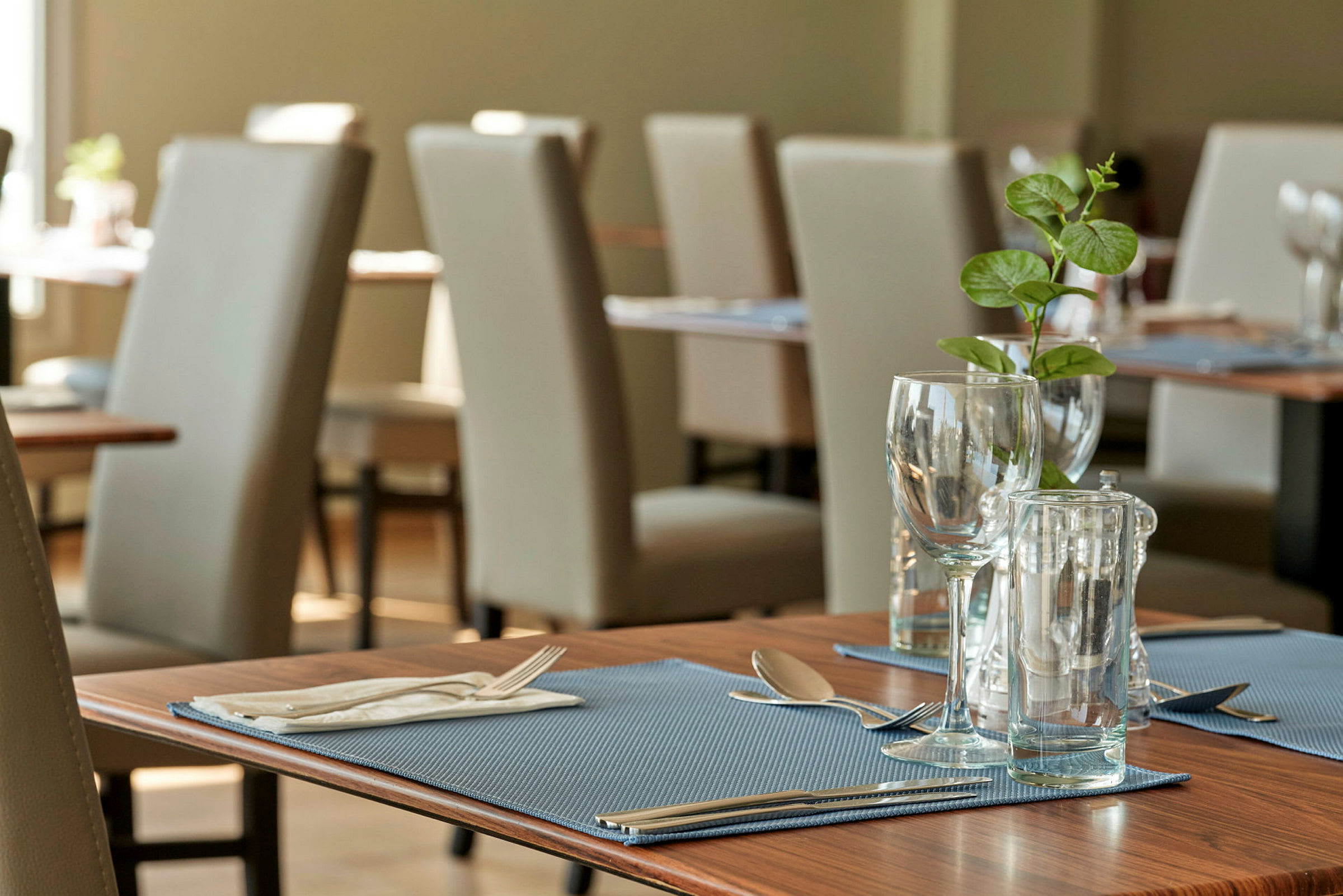 Ett dukat bord med glas, bestick och en grön växt på en restaurang. (AI-genererad text)