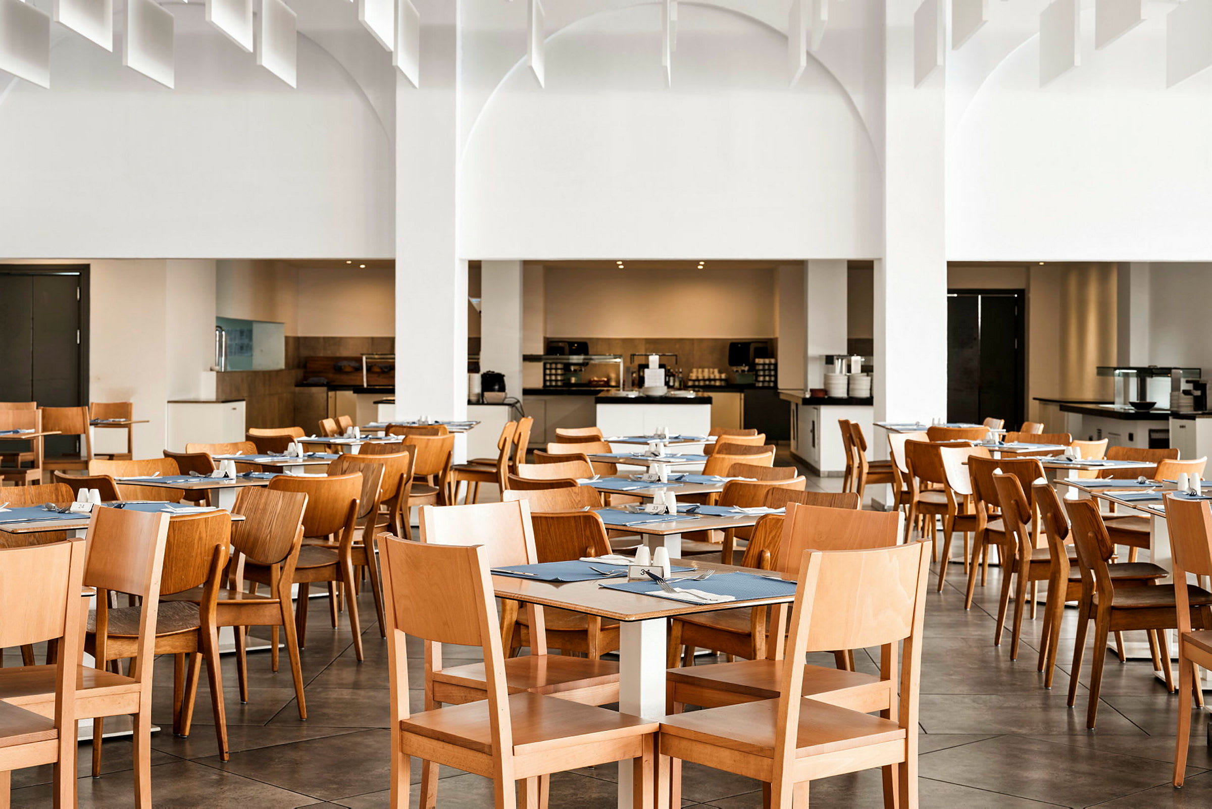 En matsal med trästolar och bord, dukade med blå bordsunderlägg. (AI-genererad text)