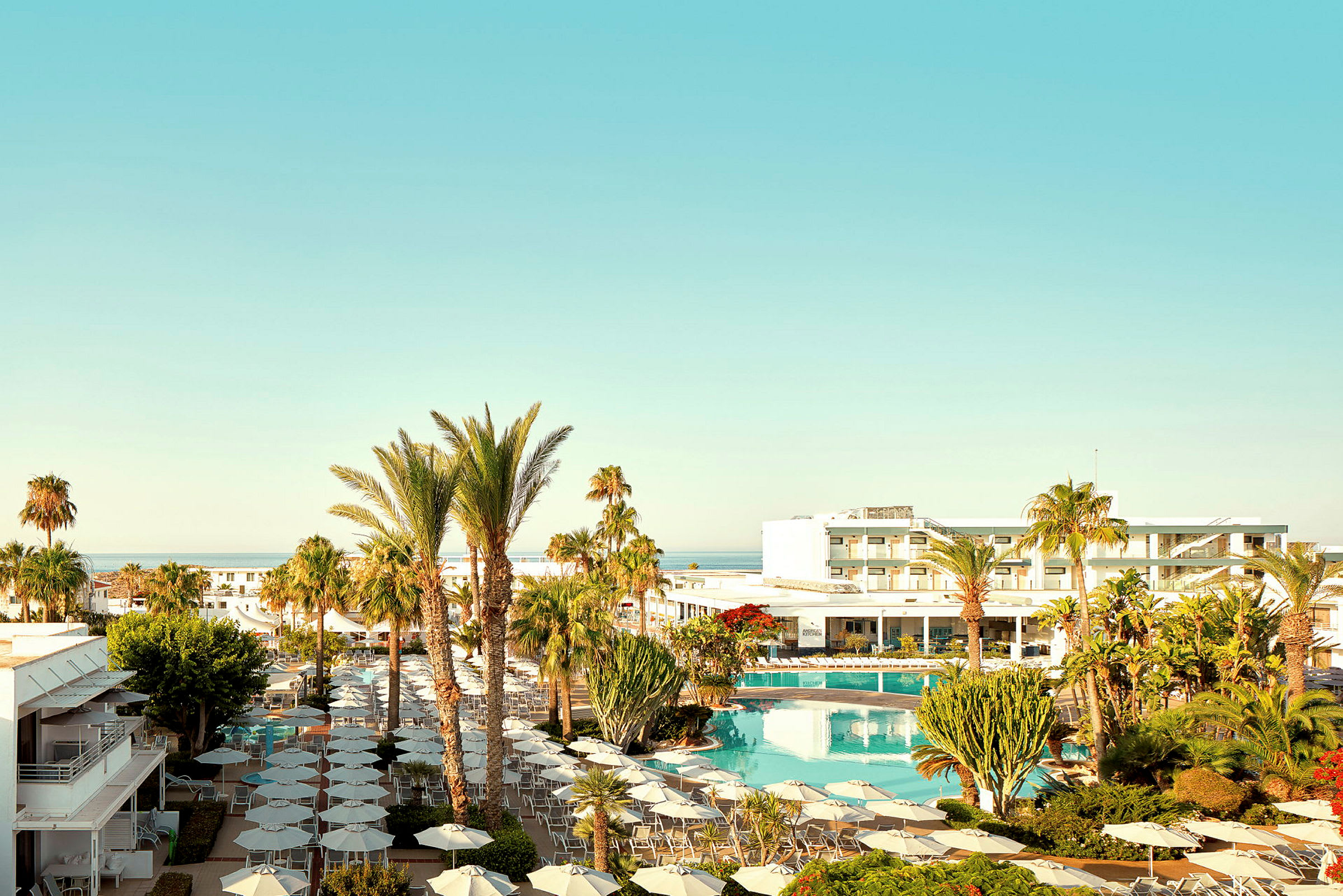 Ett hotellområde med pool, parasoller och omgivande palmer under en klarblå himmel. (AI-genererad text)