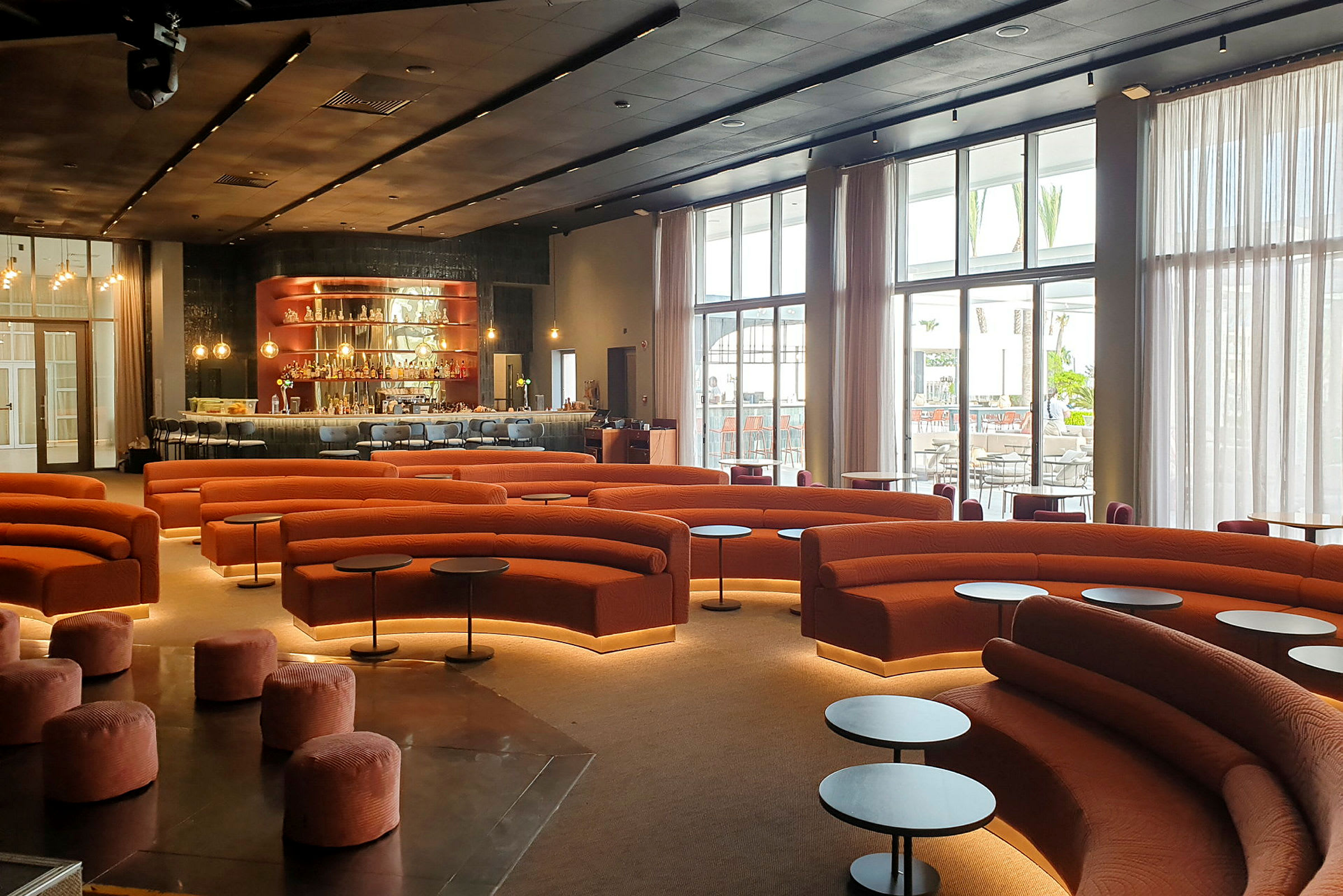 En modern lounge med orange soffor, runda småbord och en bardisk i bakgrunden. (AI-genererad text)