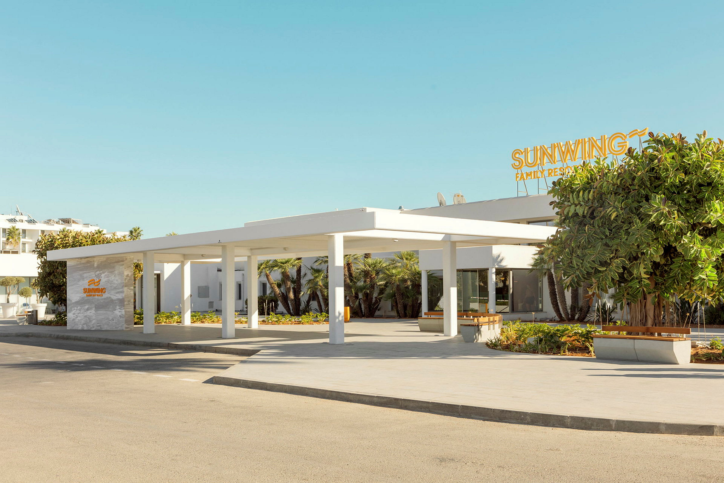 Bild av entrén till ett modernt hotell med en vit fasad och skylt med texten Sunwing Family Resort. (AI-genererad text)