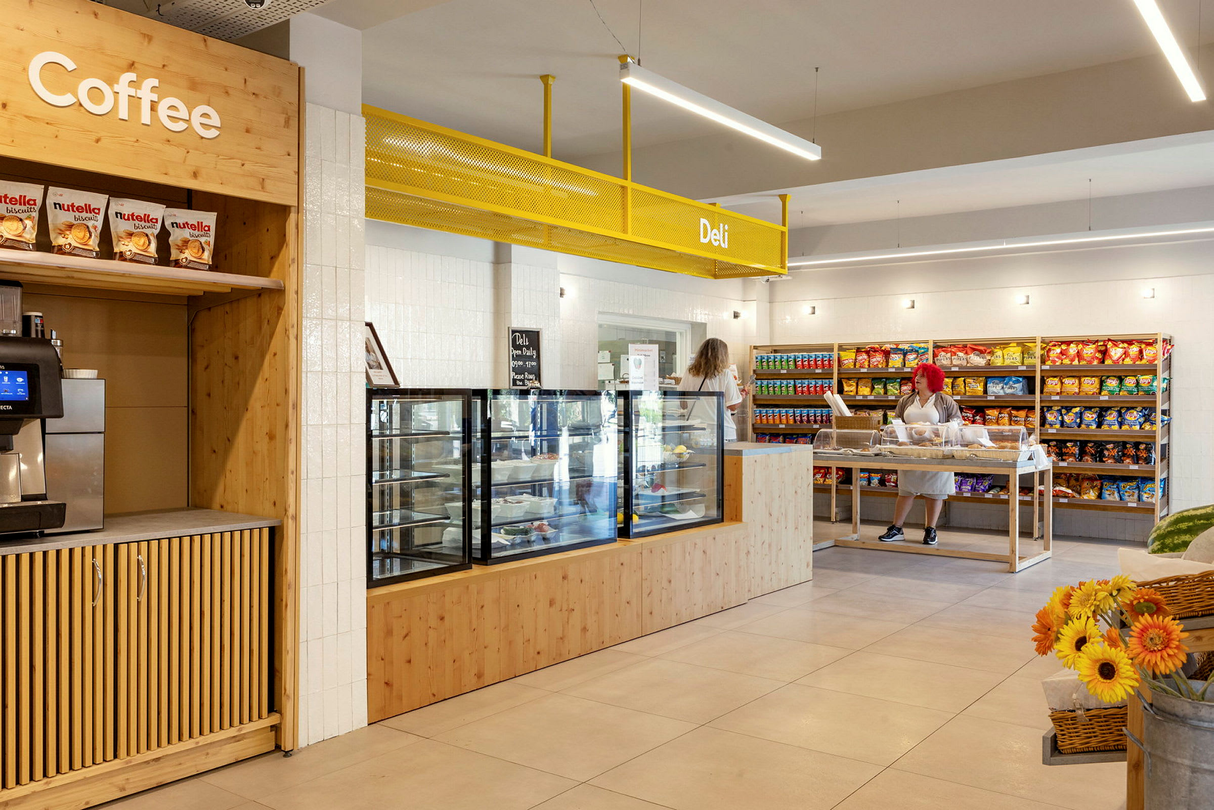 En butik interiör med en kaffestation, en disk för smörgåsar och snacks, samt hyllor fyllda med varor. (AI-genererad text)
