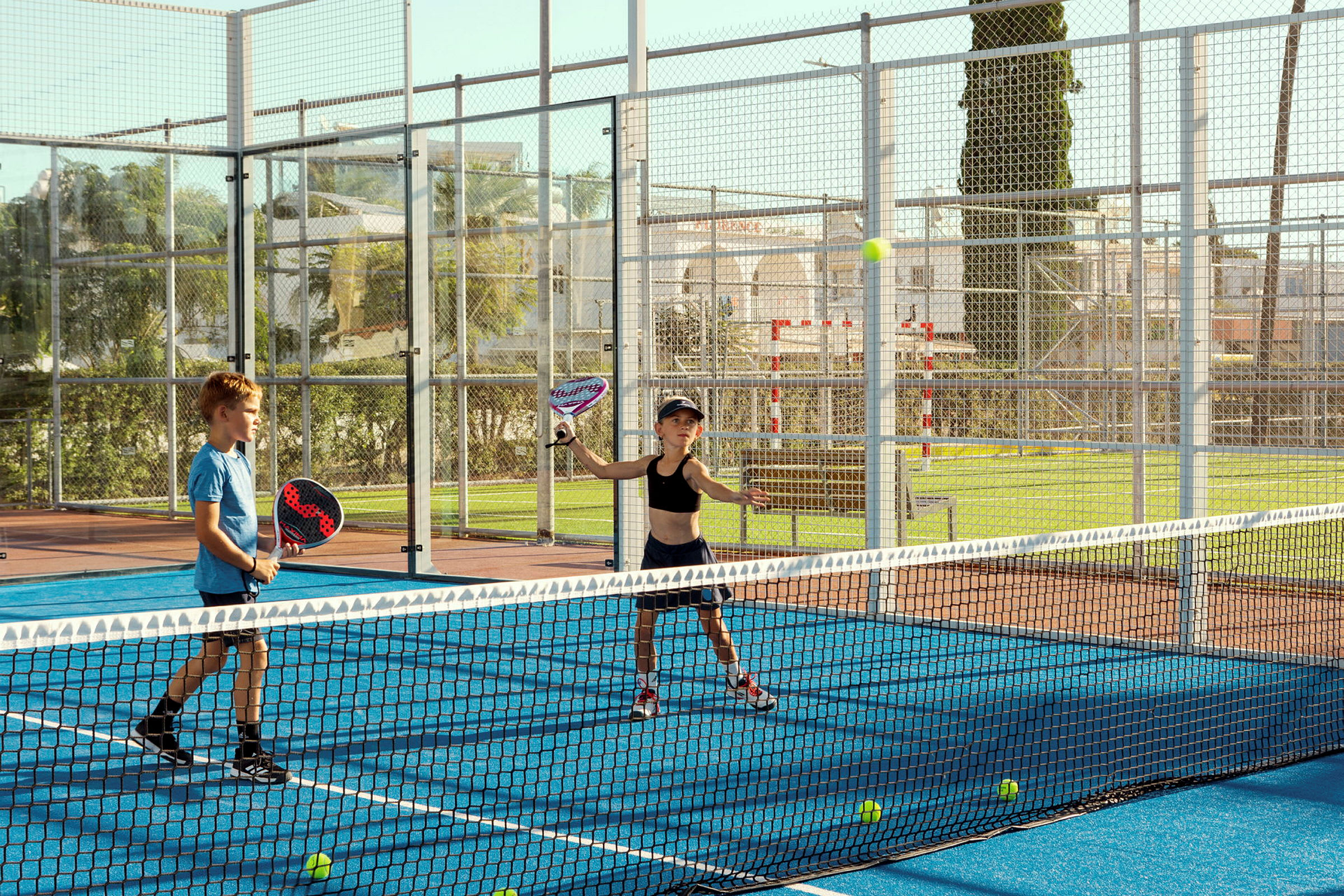 Två personer spelar padel på en blå bana utomhus. (AI-genererad text)