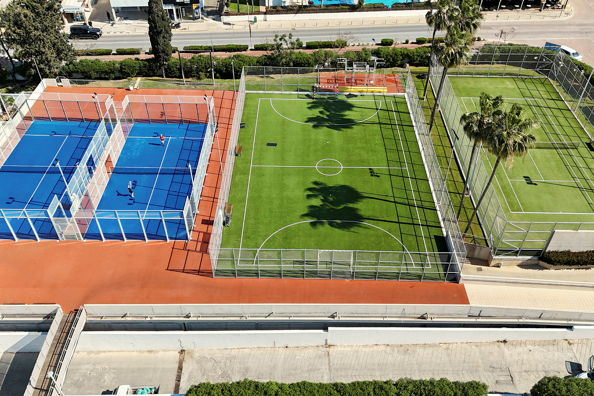Bild av flera utomhusbanor, inklusive en blå tennis- eller padelbana och en grön fotbollsplan. (AI-genererad text)