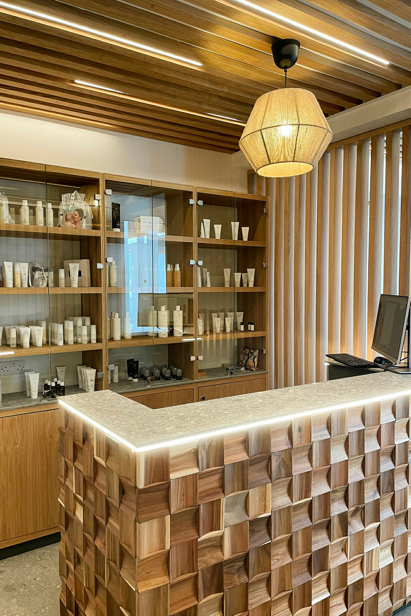 Bild av en reception med en träpanel med geometriska mönster, en disk med stenskal och hyllor i trä bakom, fyllda med produkter. (AI-genererad text)
