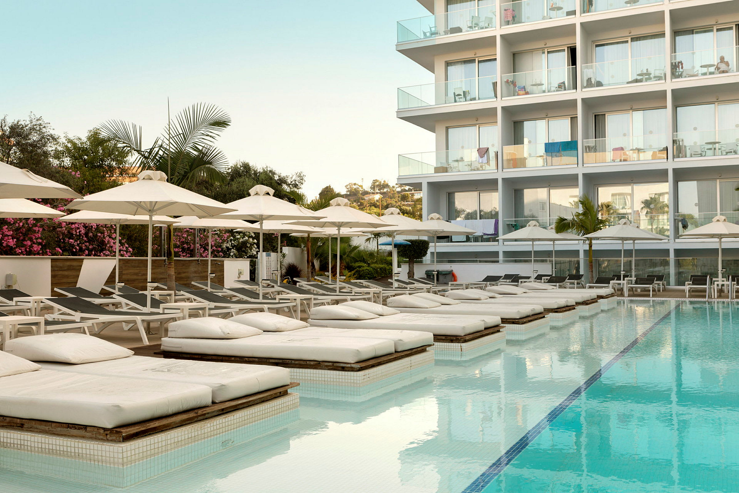 En pool med solbäddar och parasoller framför en modern byggnad. (AI-genererad text)
