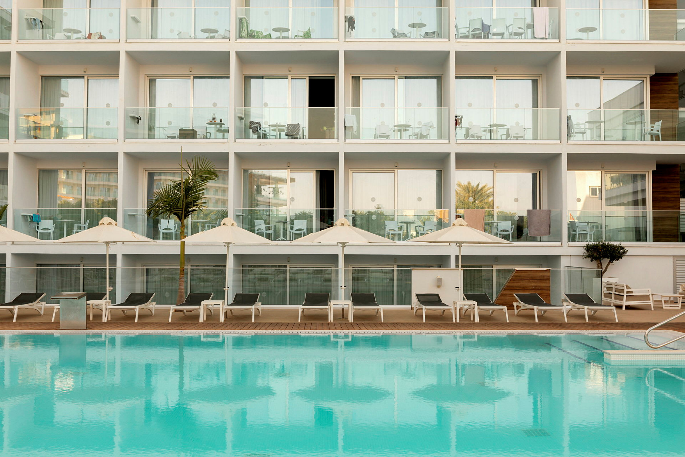 Hotellfasad med balkonger och en pool framför. (AI-genererad text)