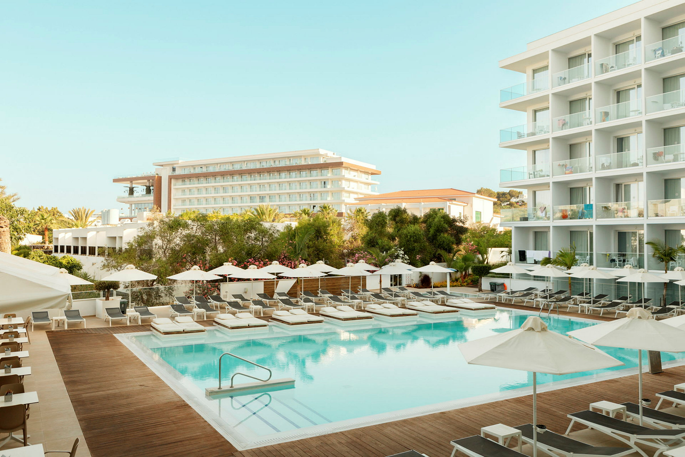 Hotellområde med pool, solstolar och byggnader i bakgrunden. (AI-genererad text)