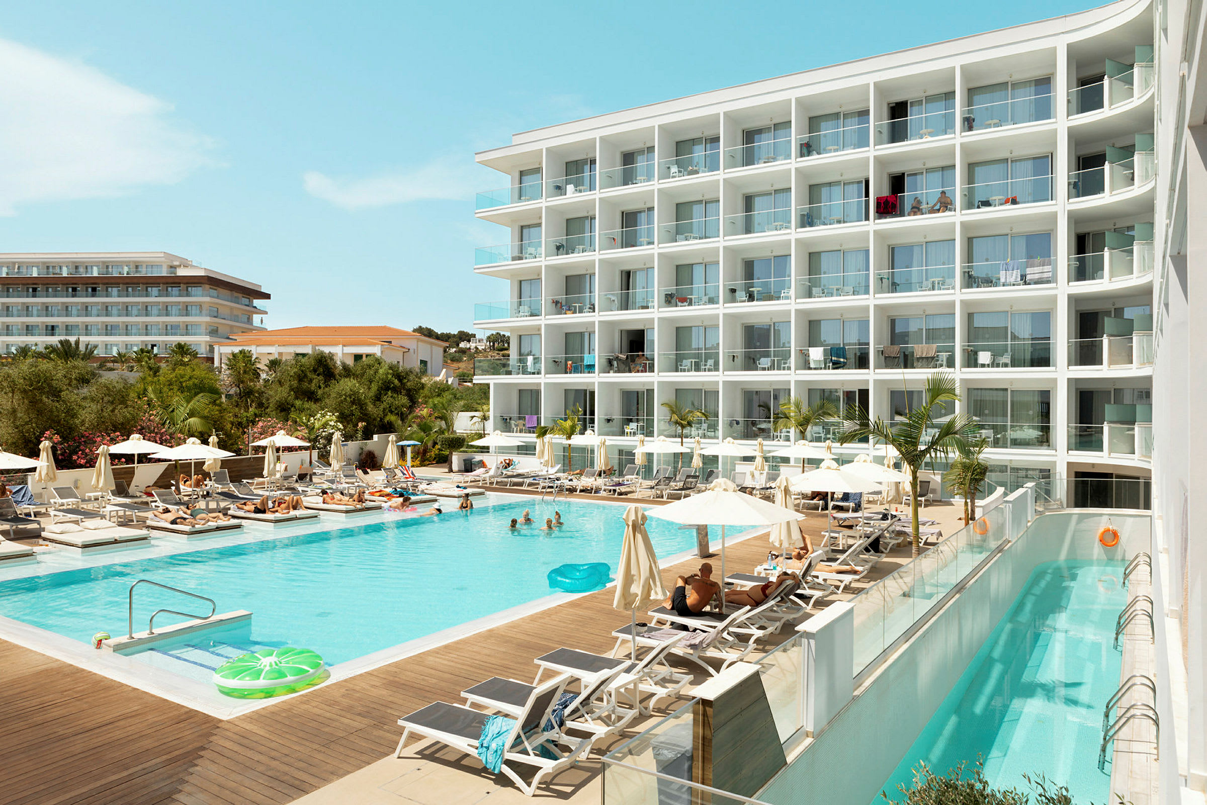 Ett hotell med en swimmingpool omgiven av solstolar och parasoller. (AI-genererad text)