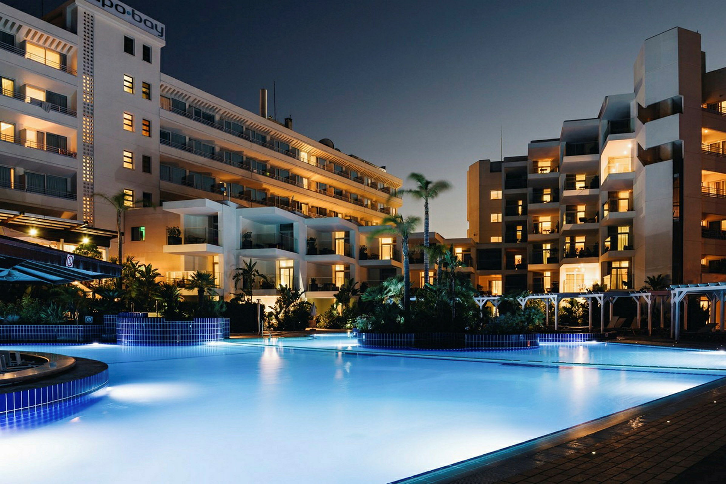 En pool framför hotellbyggnader under kvällstid. (AI-genererad text)