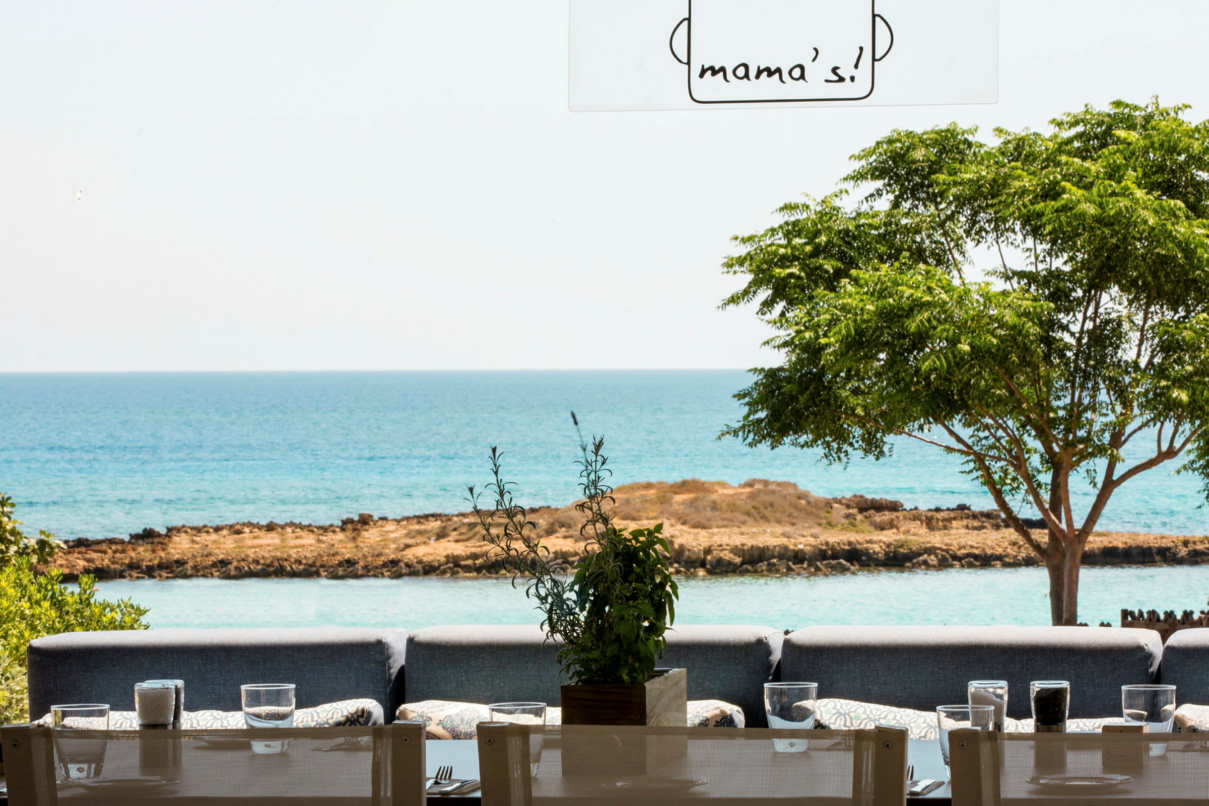 Restaurang med sittplatser utomhus, utsikt mot havet och grönska. (AI-genererad text)