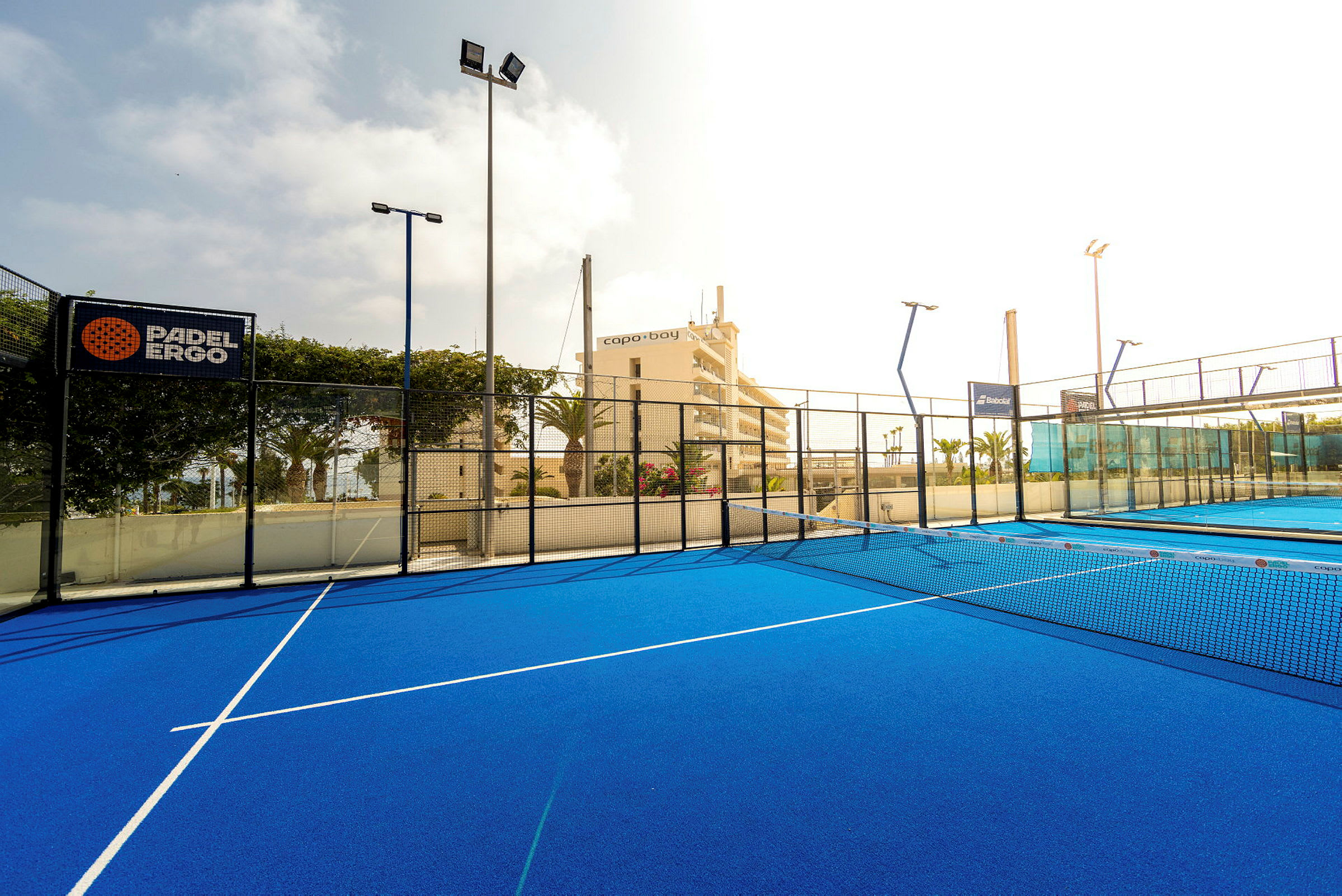 En padel-plan med blått underlag och nät samt omgivande staket. (AI-genererad text)