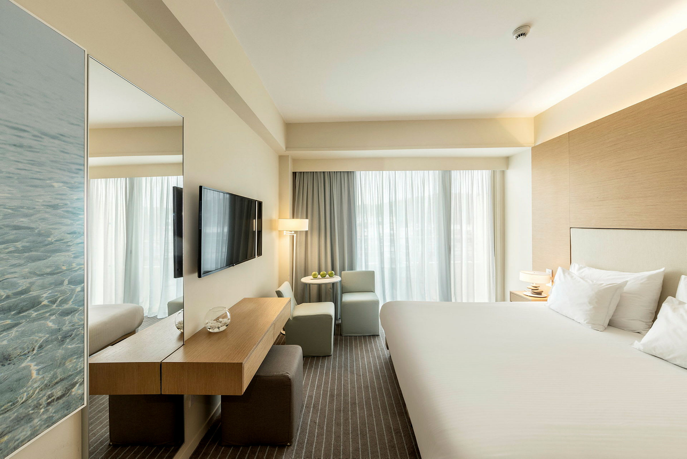 Hotellrum med en stor säng, TV på väggen och sittgrupp vid fönstret. (AI-genererad text)