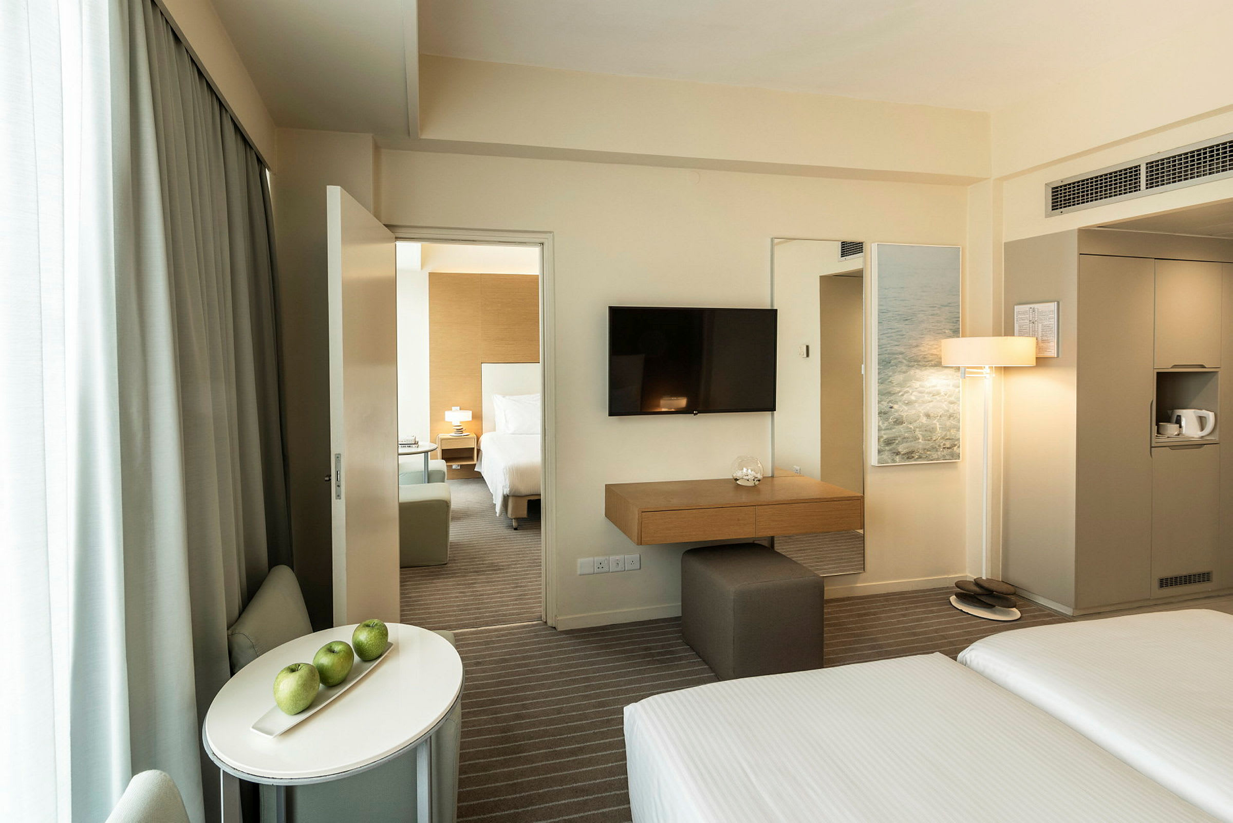 Hotellrum med säng, soffa och bord med tre gröna äpplen. (AI-genererad text)