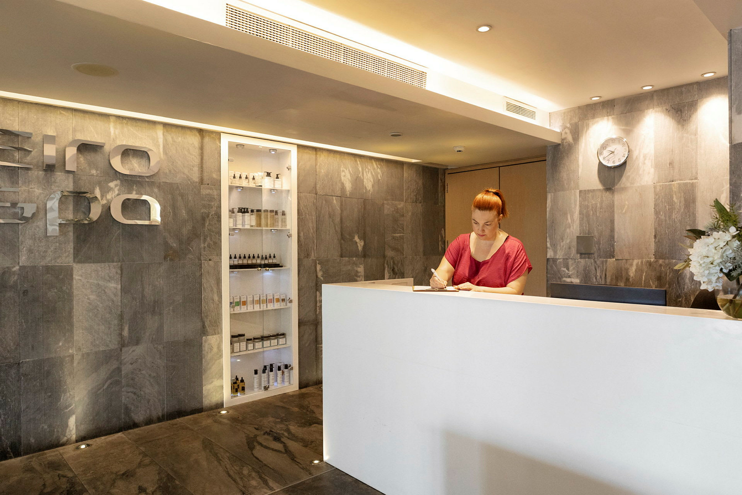 Receptionen i en spa-anläggning med en vit disk och vägg av sten. (AI-genererad text)