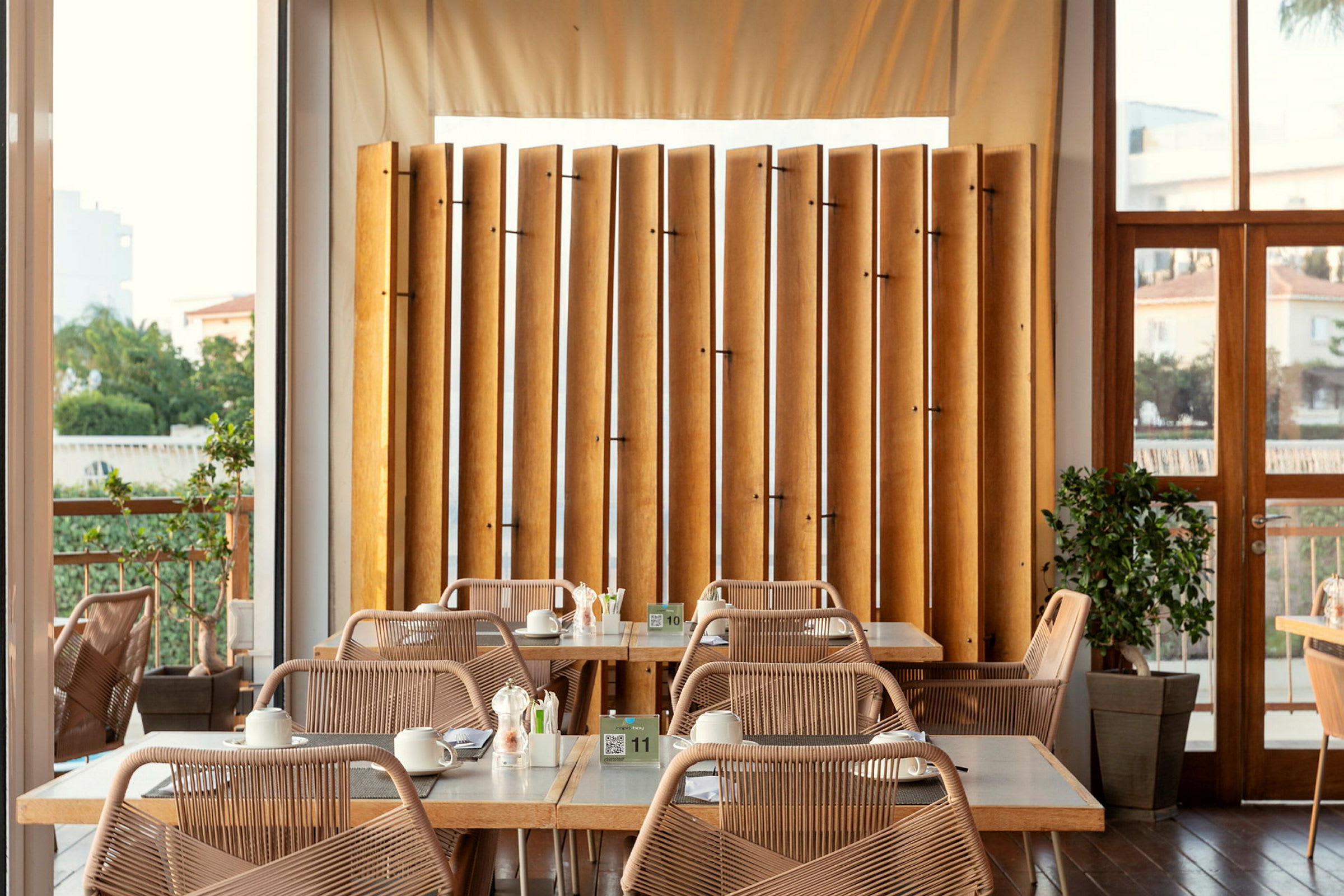 En ljus restaurang med bord och stolar samt träd vågrätt utplacerade. (AI-genererad text)