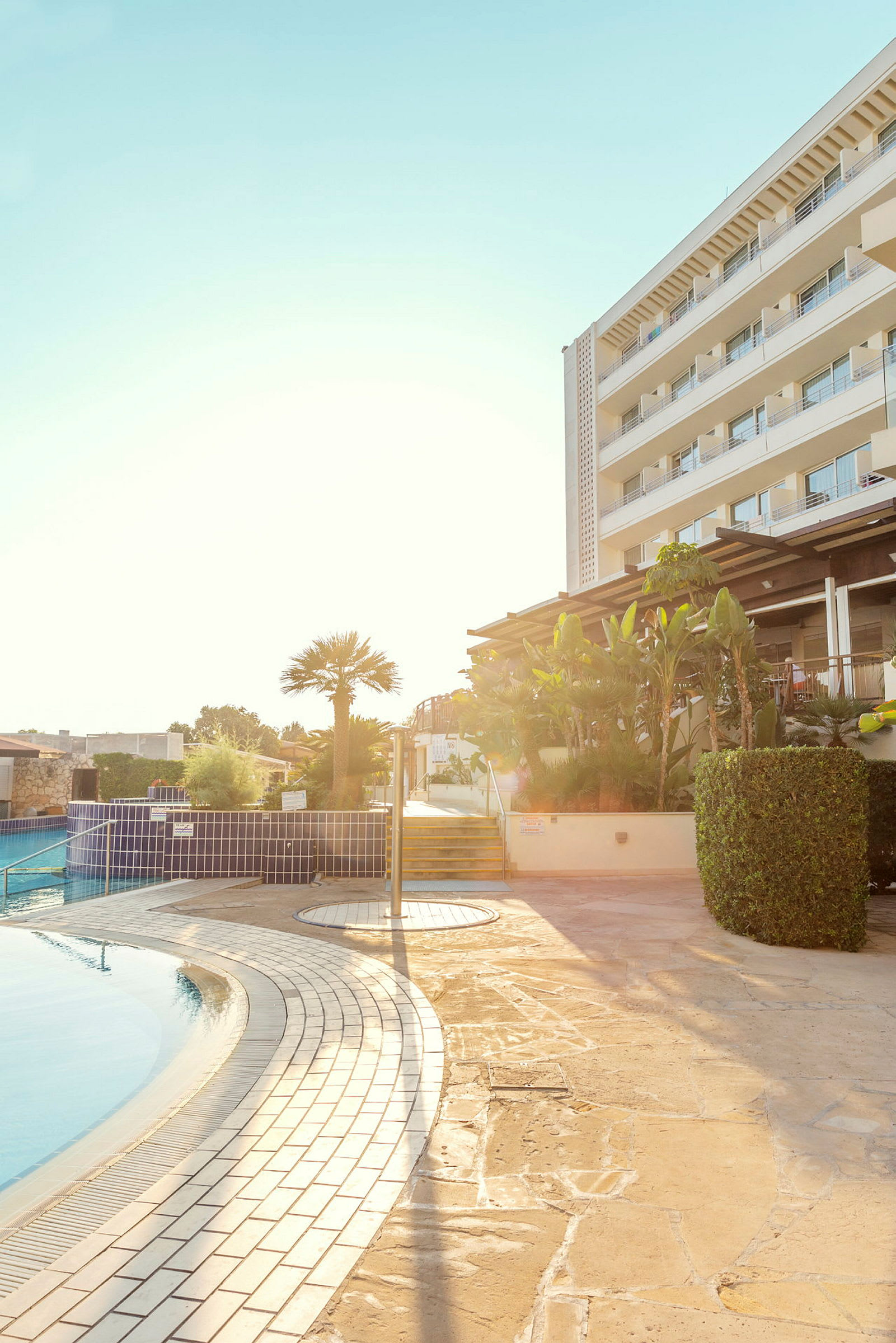 Hotell med poolområde och en anlagd miljö i solljus. (AI-genererad text)