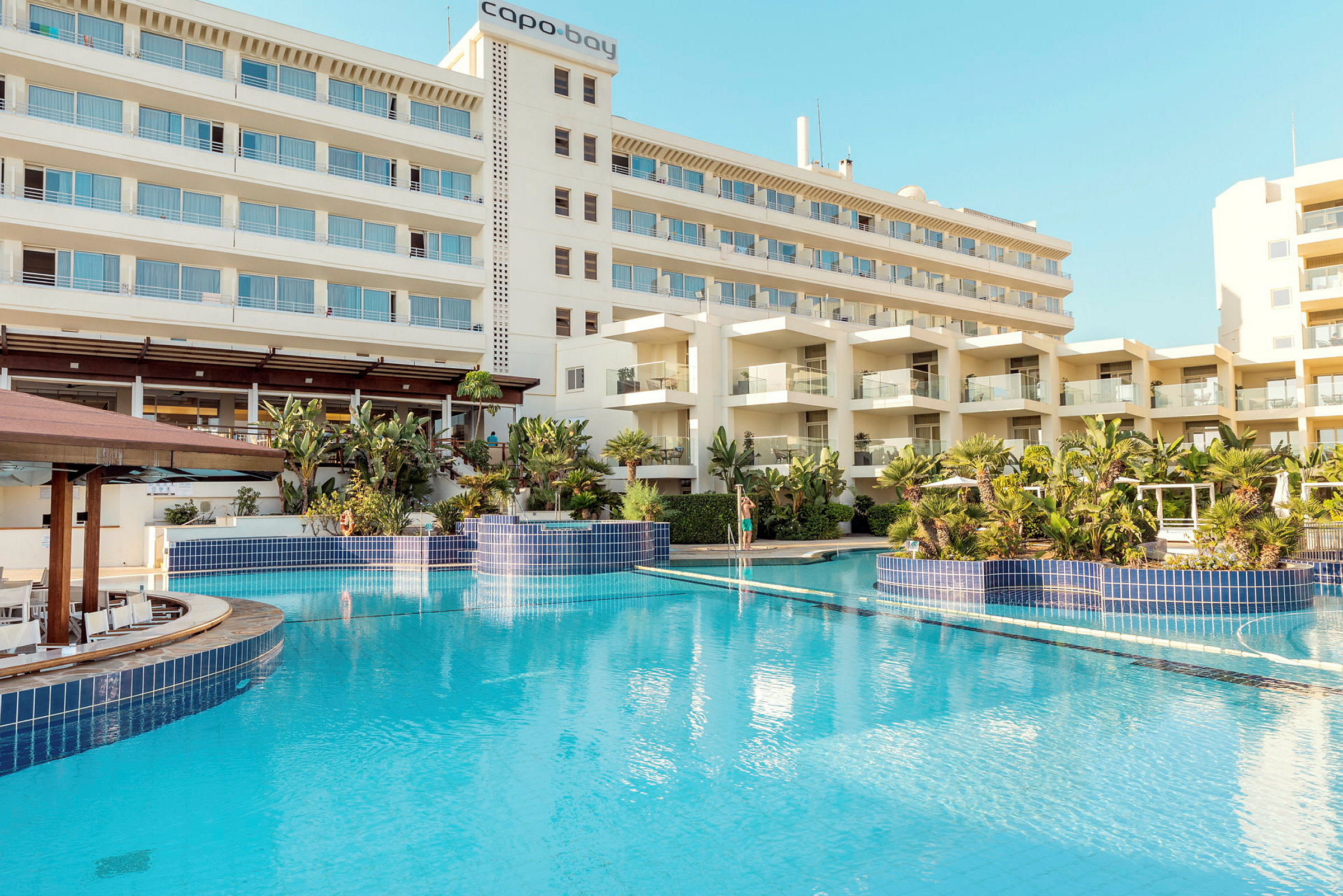 Hotellbyggnad med flera våningar och en stor blå pool omgiven av växtlighet. (AI-genererad text)