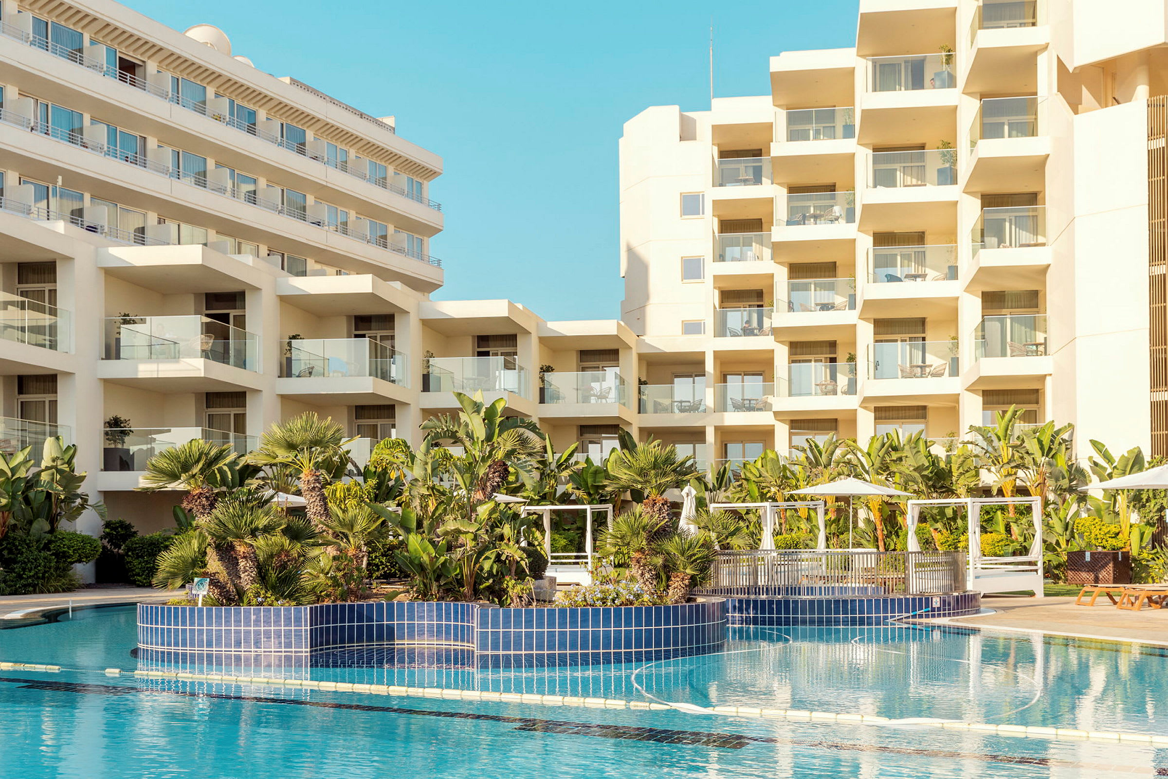 Bild av hotellbyggnader med en pool och frodig grönska i förgrunden. (AI-genererad text)