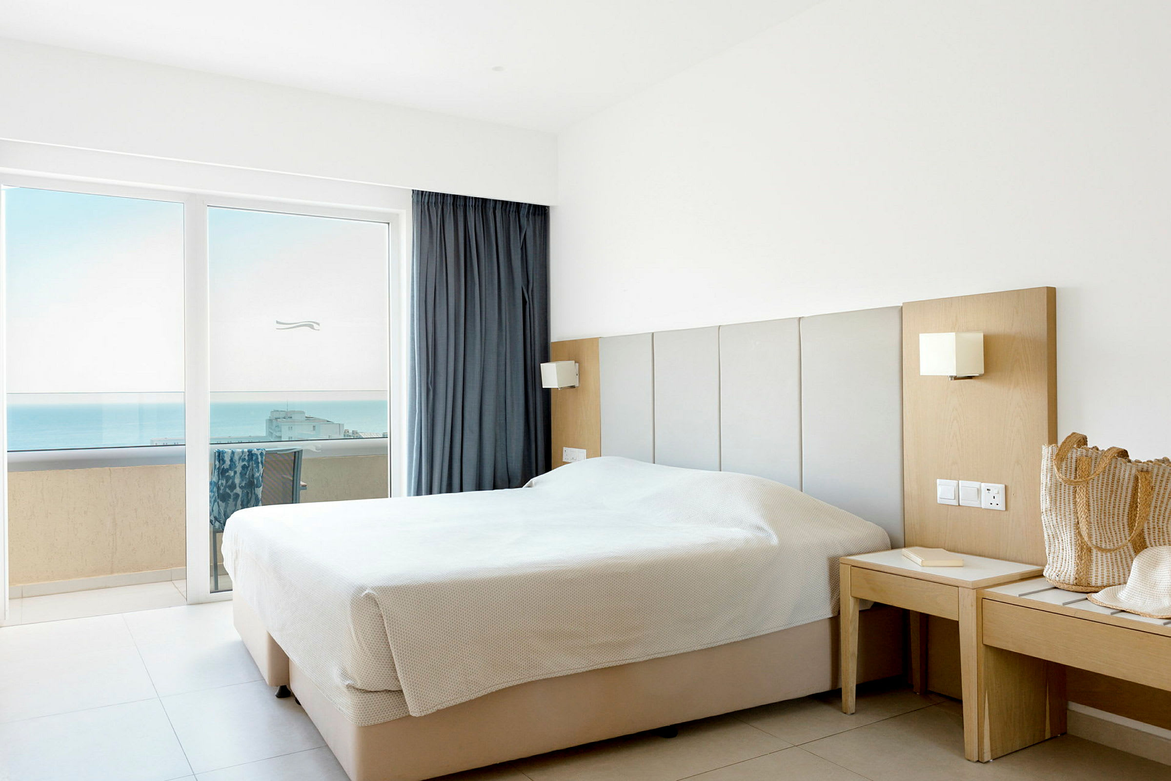 Ett hotellrum med en dubbelsäng nära fönster med utsikt över havet. (AI-genererad text)