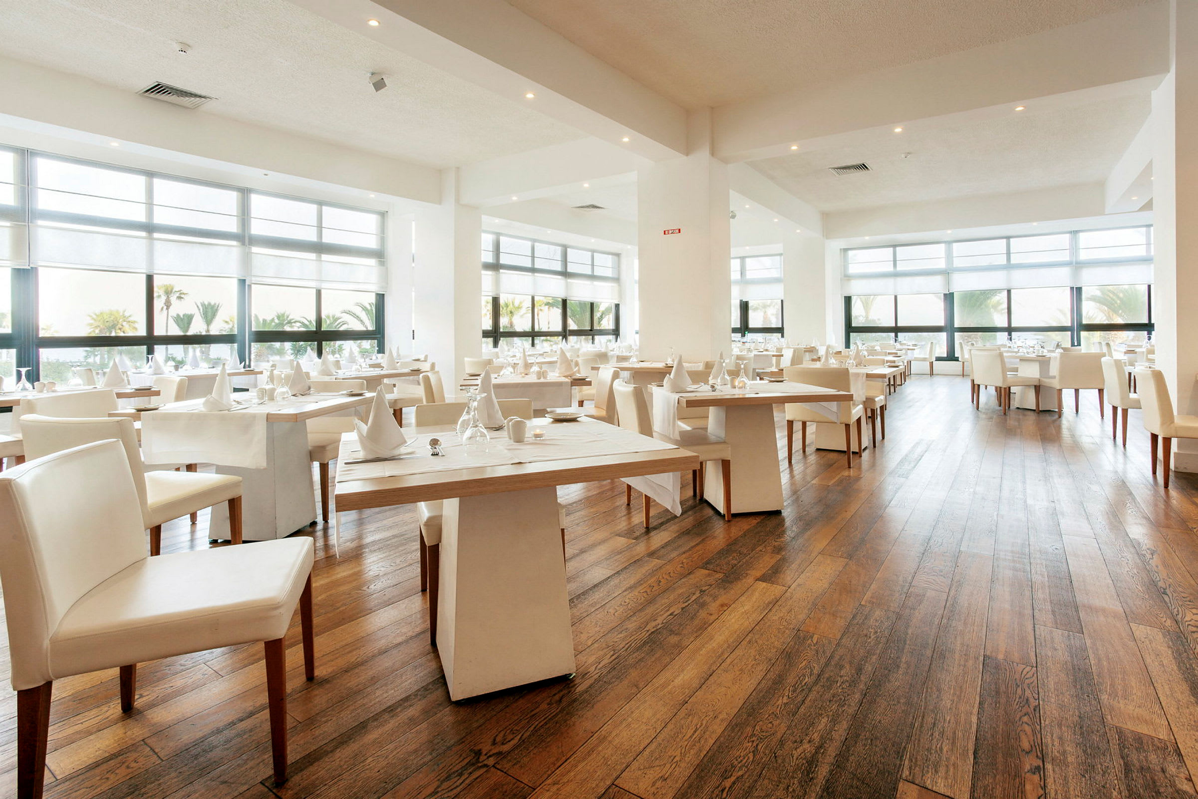 En modern och ljus restaurang med stora fönster och dukade bord. (AI-genererad text)