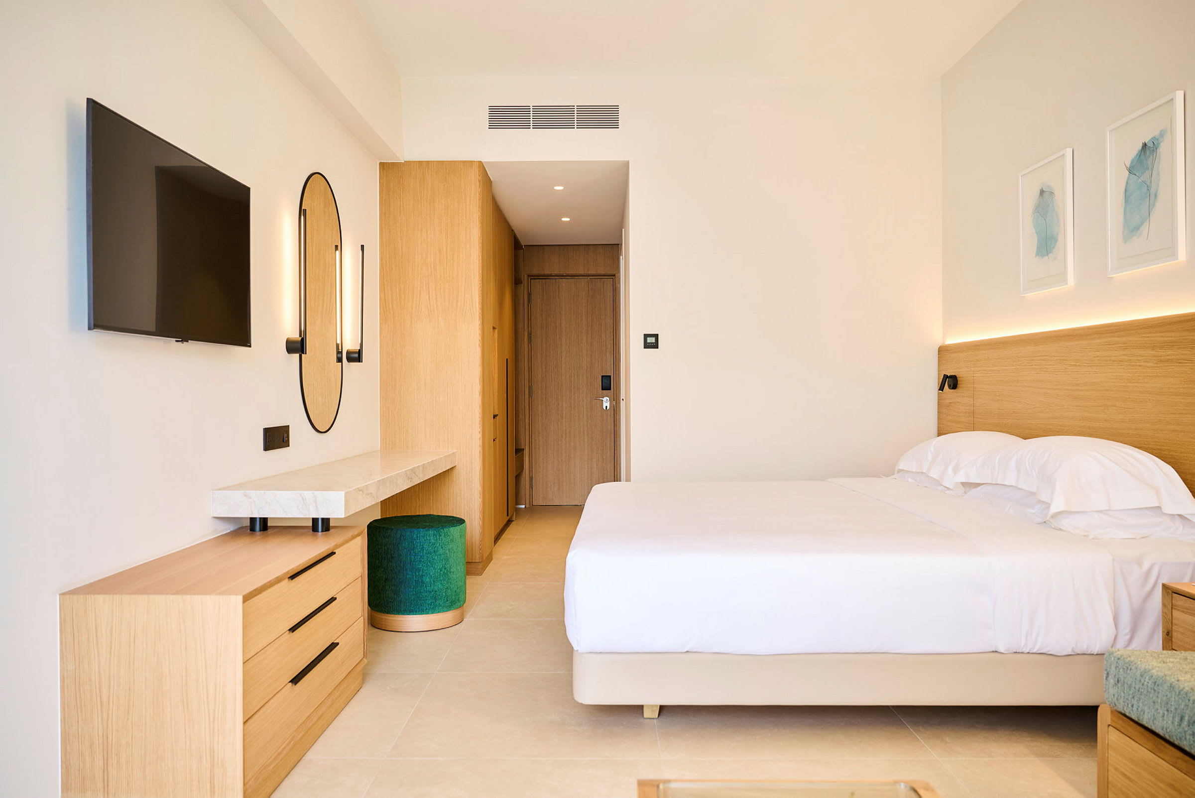 Ett hotellrum med en dubbelsäng, väggmonterad TV, spegel och träinredning. (AI-genererad text)