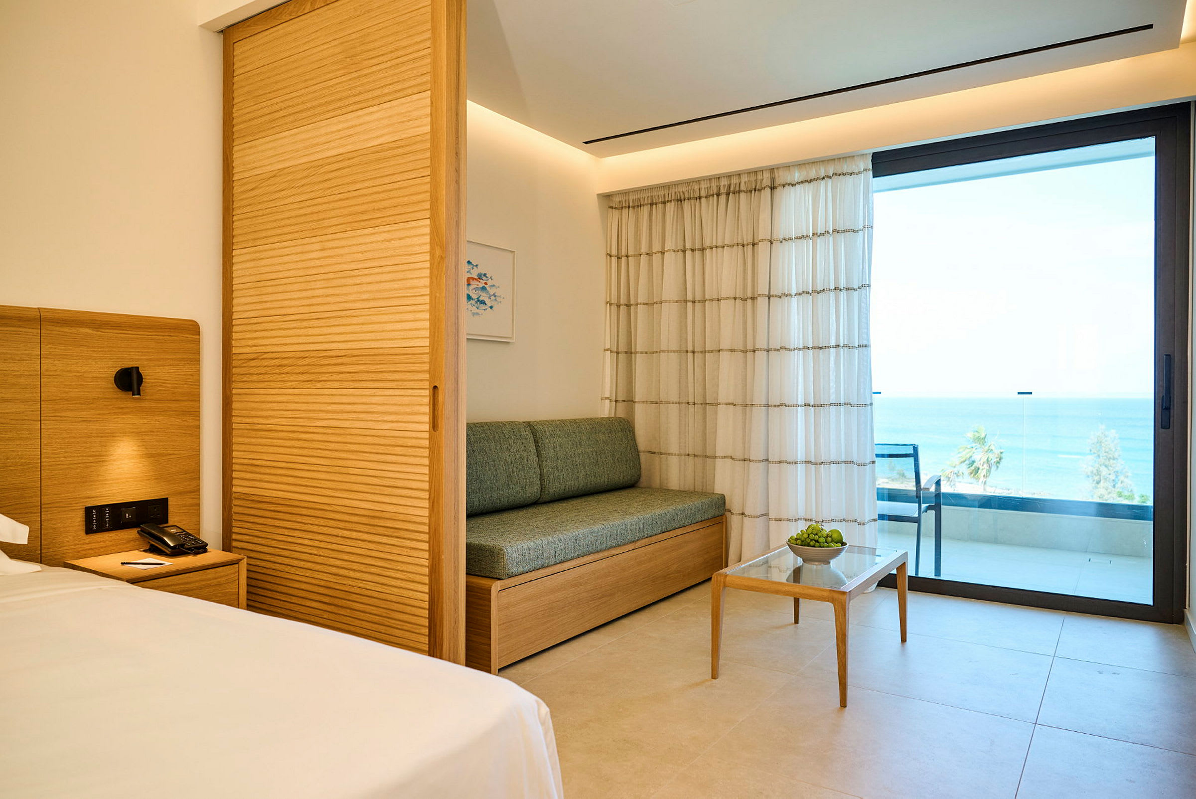 Ett hotellrum med modern inredning, en soffa, ett litet bord och en balkong med havsutsikt. (AI-genererad text)