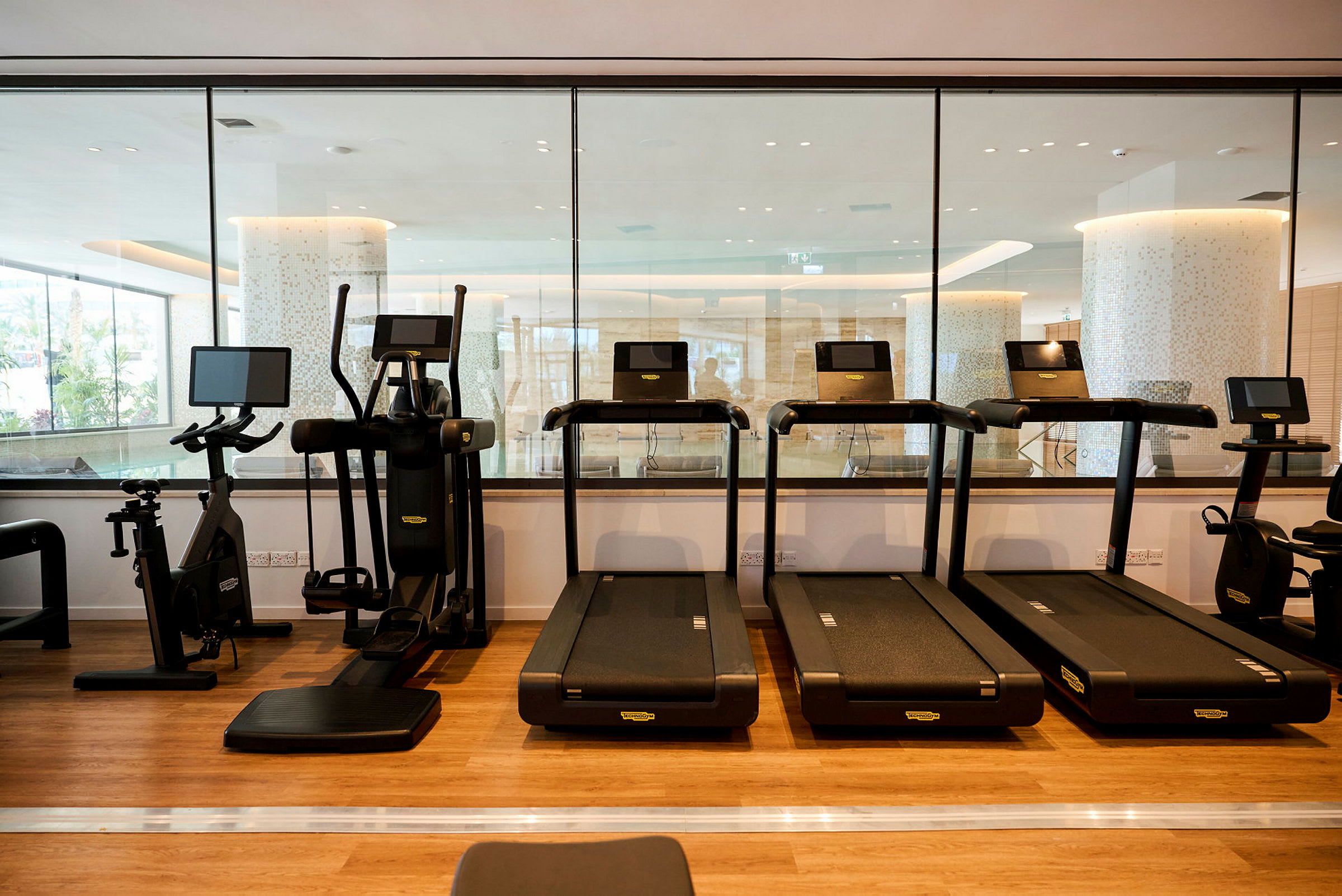 Ett gym med flera löpband och träningsmaskiner på ett golv av trä. (AI-genererad text)