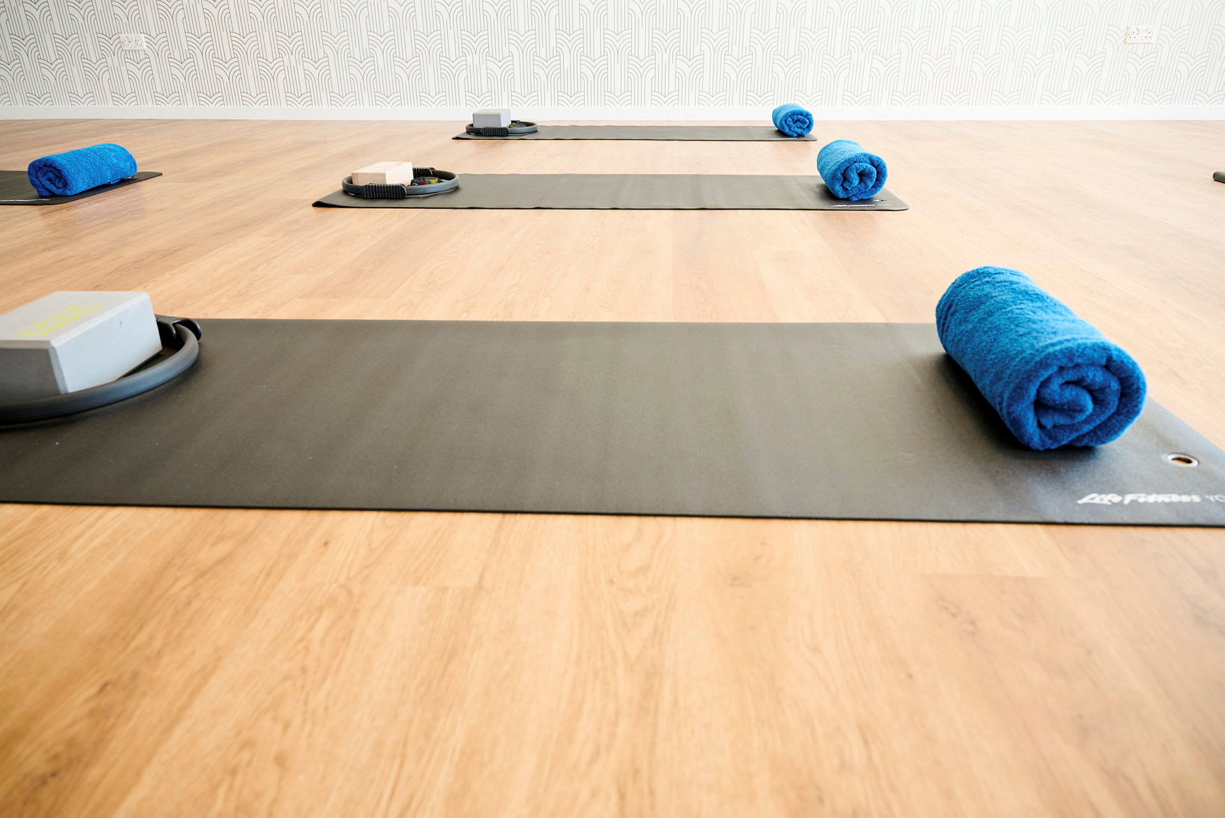 Bild av en träningsstudio med yogamattor, blå handdukar och träningsblock på ett trägolv. (AI-genererad text)