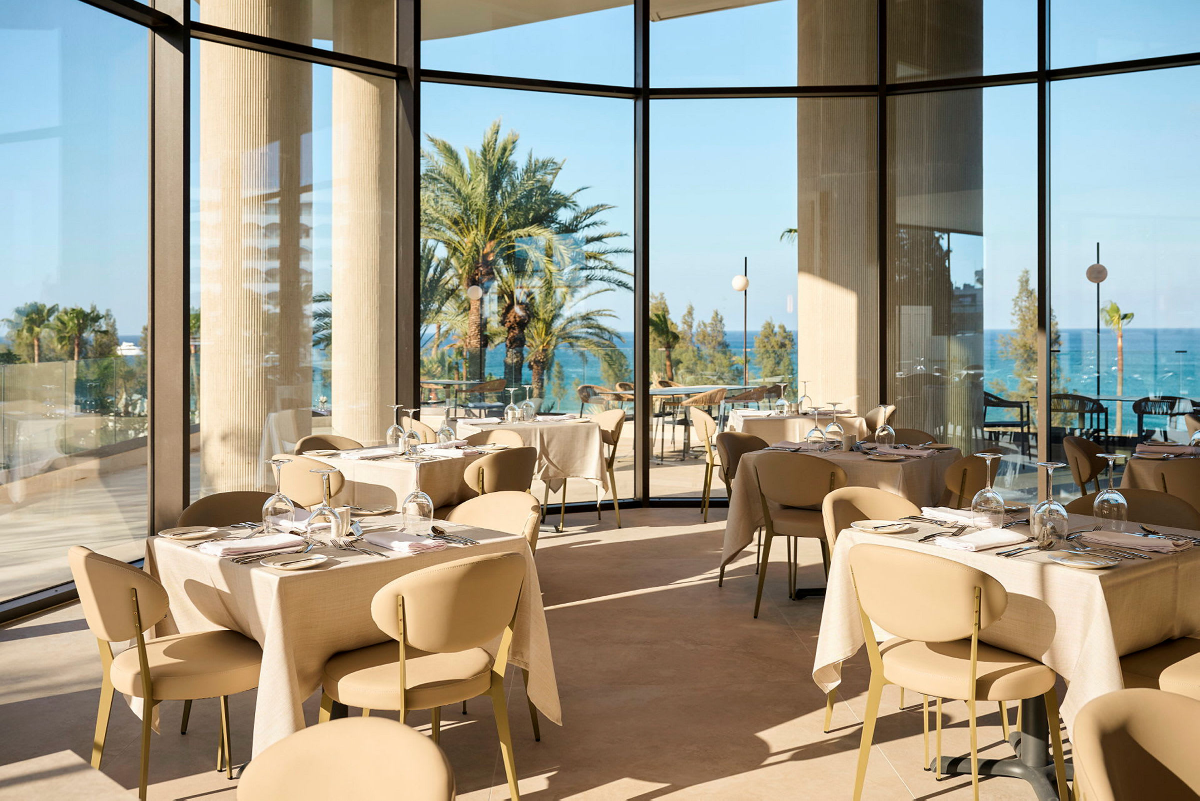 En ljus och elegant restaurang med panoramafönster som visar utsikt över palmer och hav. (AI-genererad text)