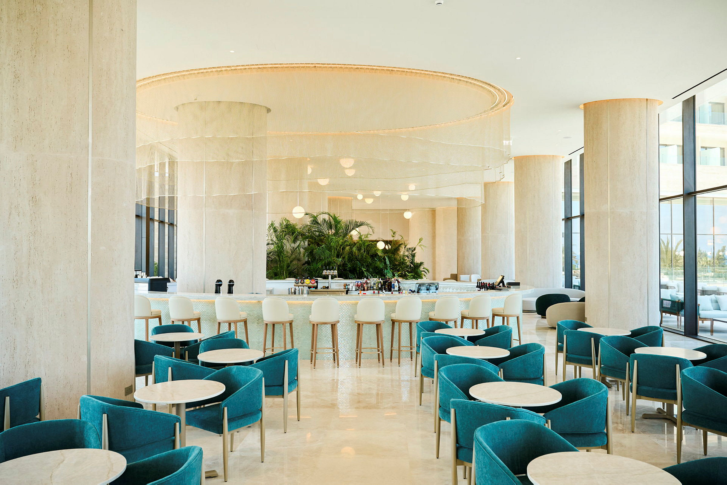 En modern hotellbar med turkosa stolar och runda bord, en elegant bardisk i bakgrunden och stora fönster som släpper in dagsljus. (AI-genererad text)