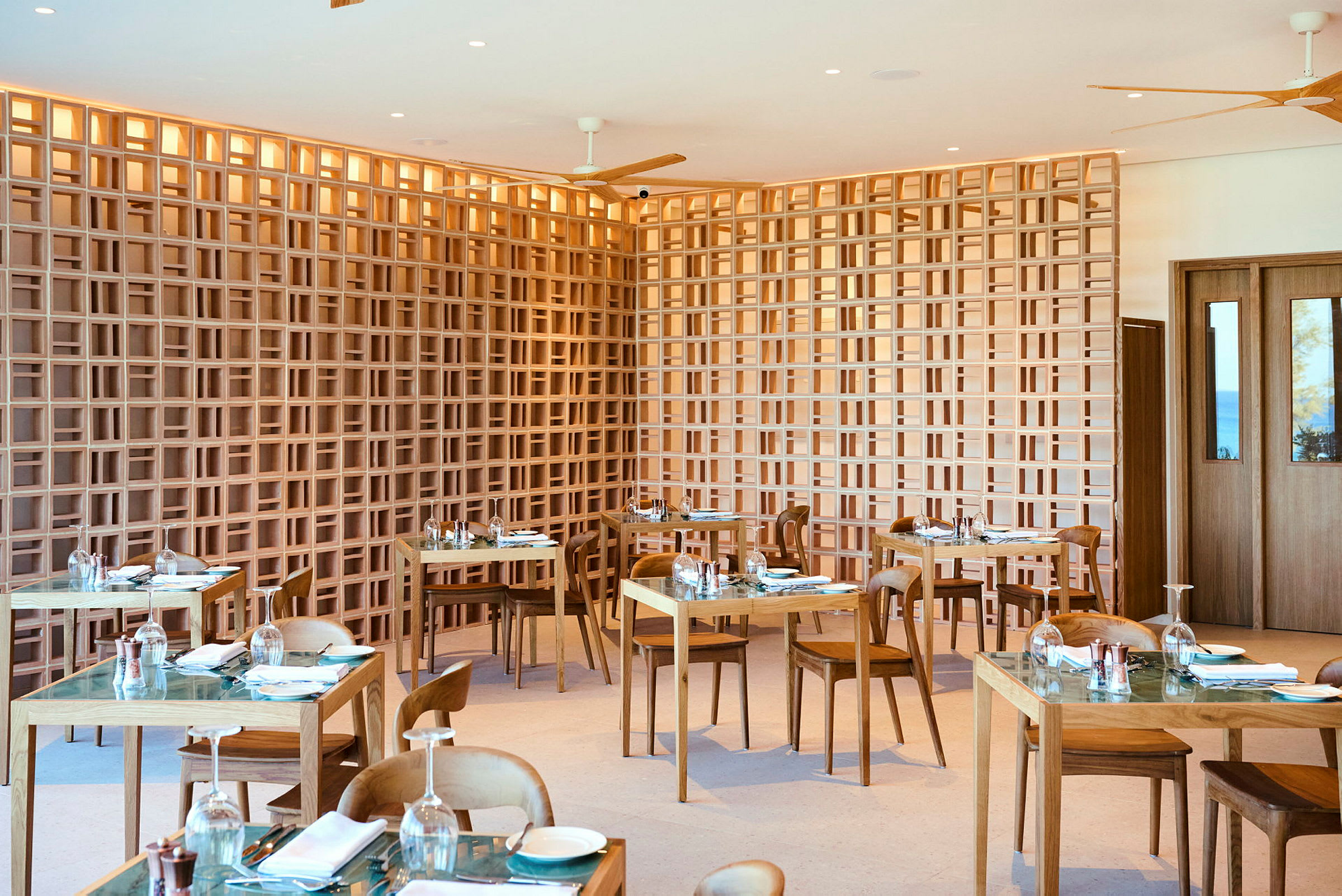 Ett modernt restaurangområde med träbord och stolar samt en dekorativ gallerliknande trävägg. (AI-genererad text)