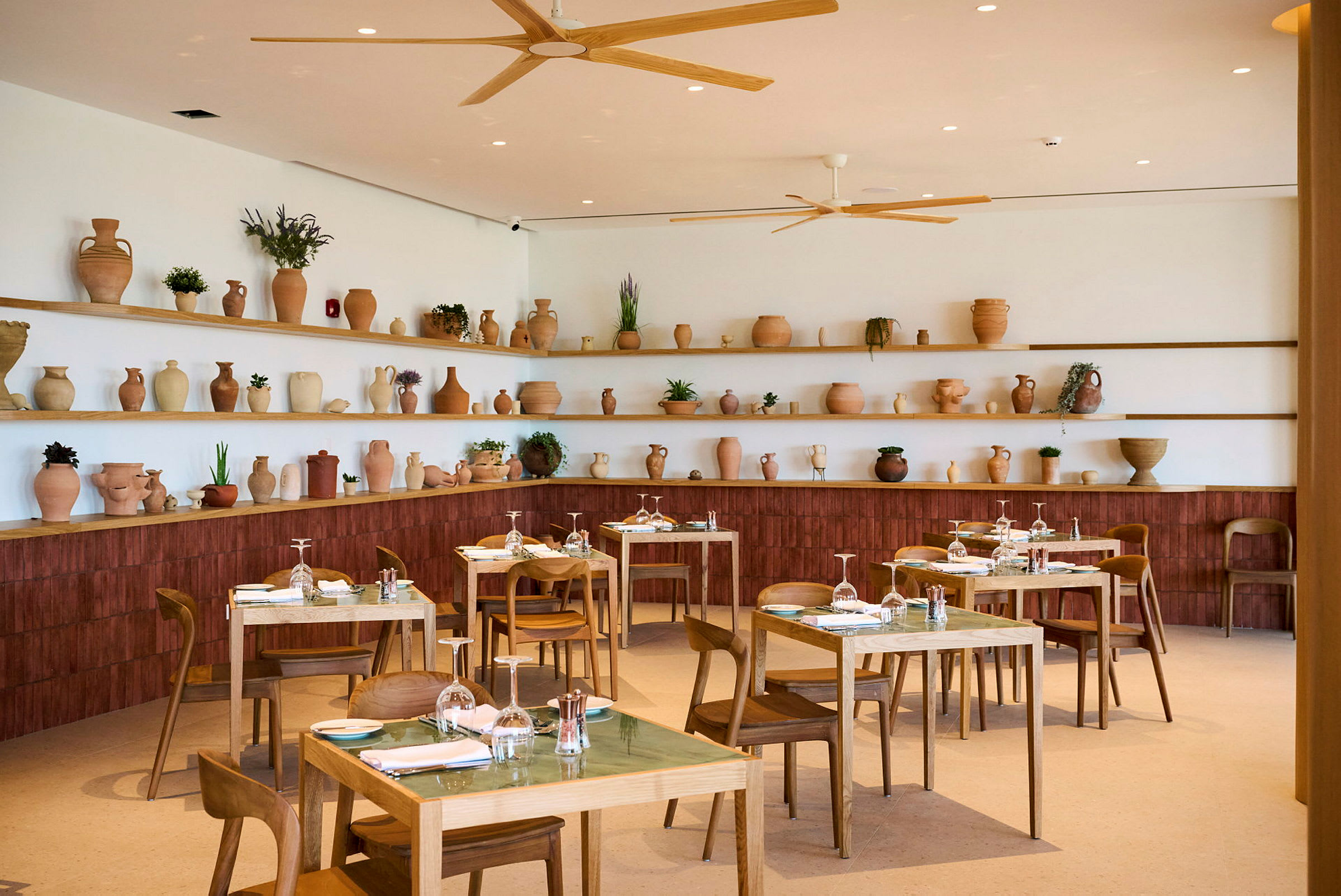 Bild av en restauranginteriör med träbord och stolar. Hyllor på väggen bakom är dekorerade med terrakottakrukor och växter. (AI-genererad text)