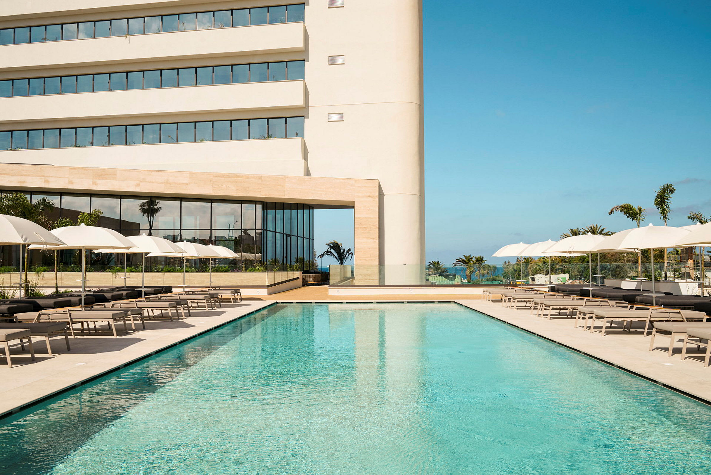 Hotell med pool, solstolar och parasoller framför en modern byggnad. (AI-genererad text)