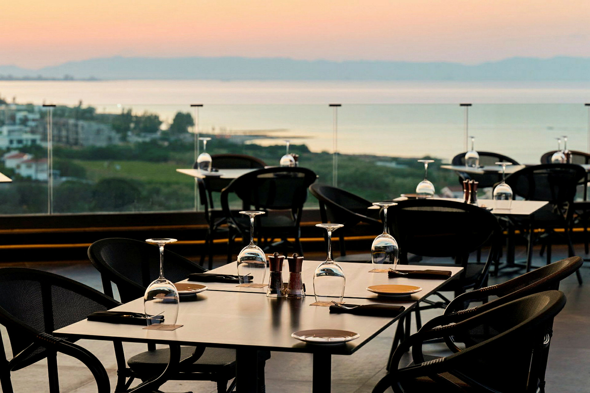 En utomhusrestaurang med dukade bord och utsikt över landskap och vatten. (AI-genererad text)