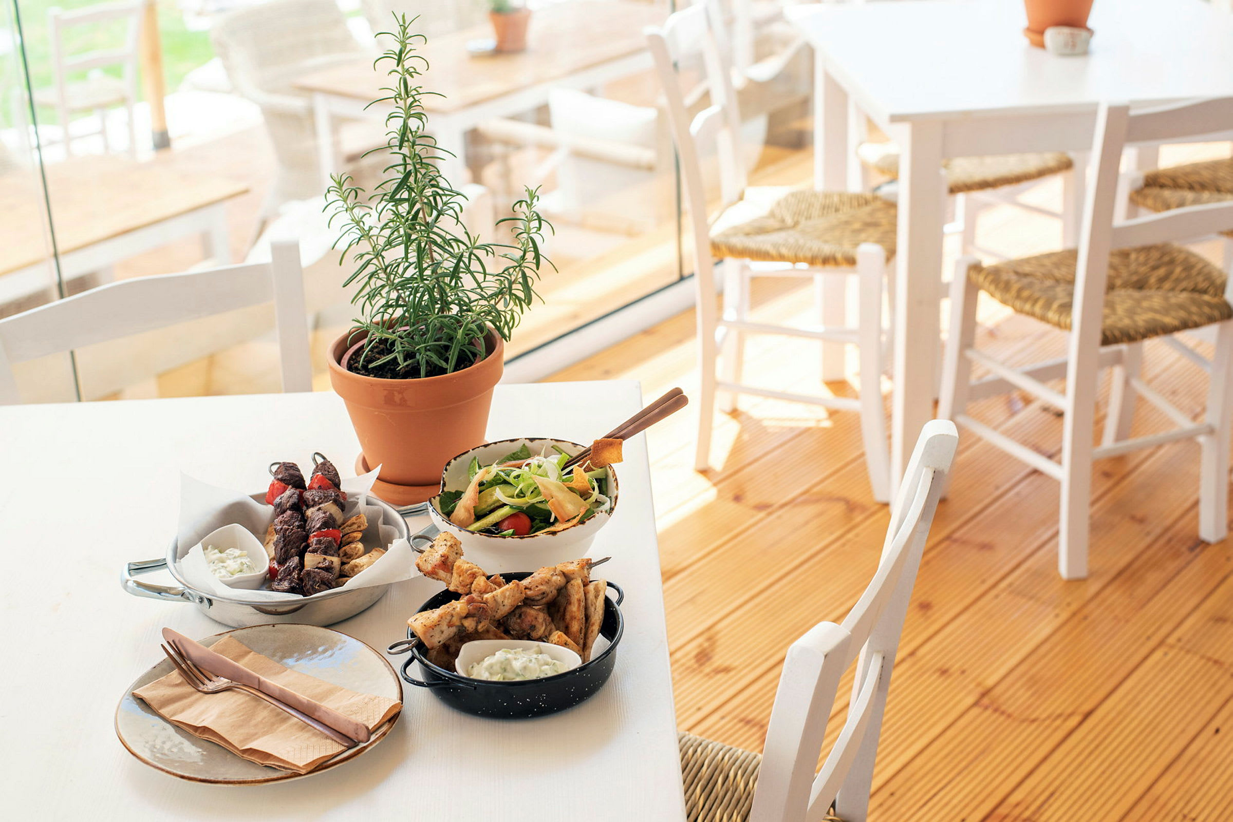 En dukad bord med olika maträtter, inklusive sallad, grillspett och en örtplanta. (AI-genererad text)