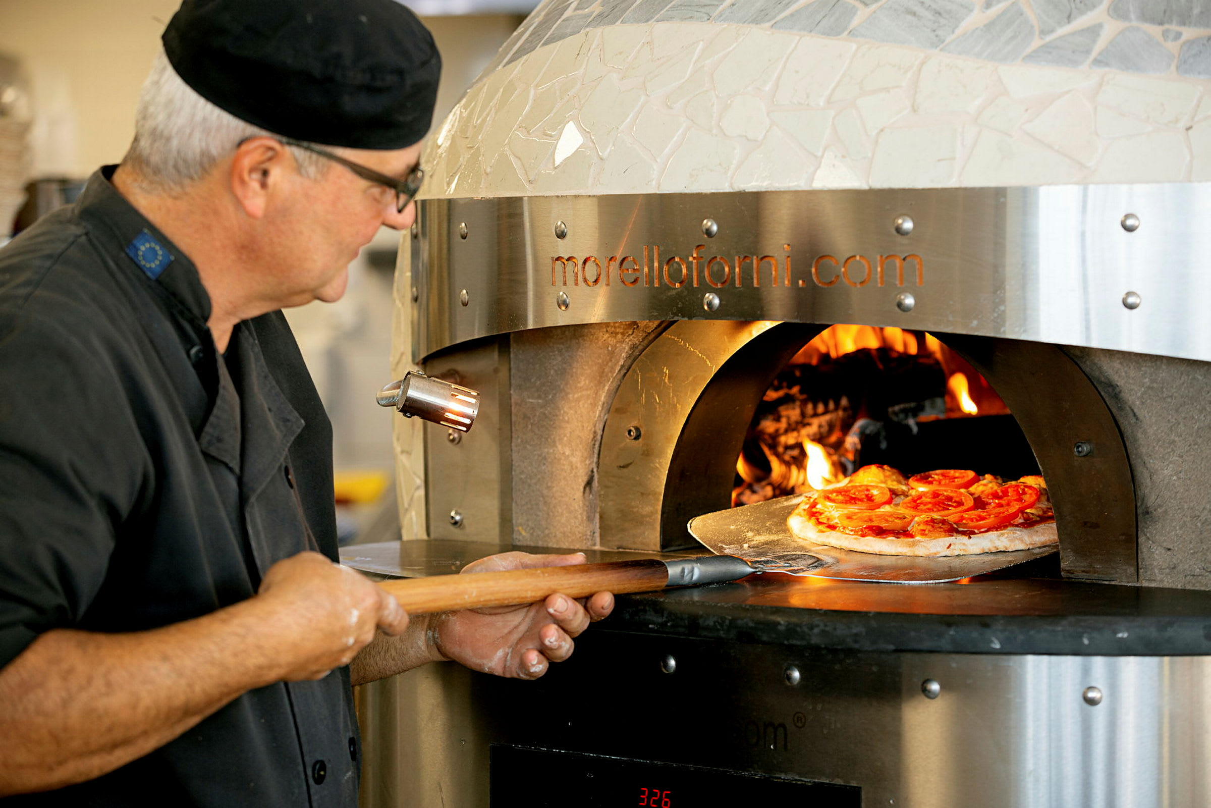 En pizza placeras i en vedeldad ugn med en pizzaspade. (AI-genererad text)